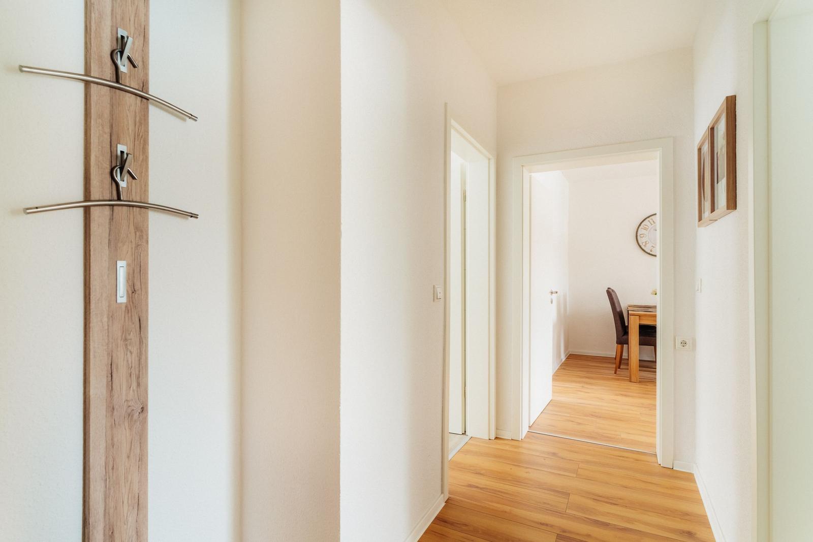 Flur mit Holzboden und Garderobenstange. Durchgang zu Esszimmer mit Tisch und Stuhl.