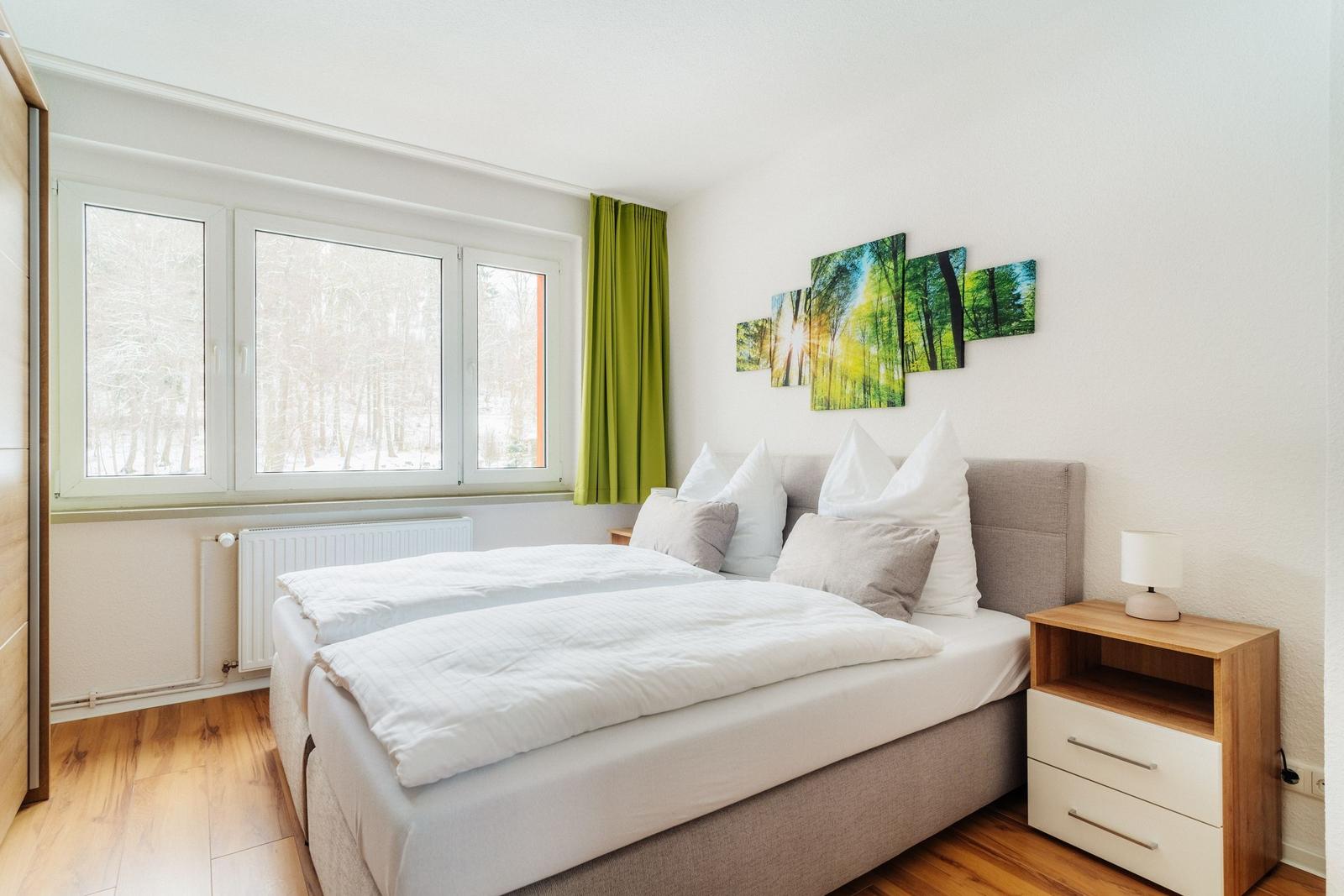 Schlafzimmer mit Doppelbett, Fensterblick auf Wald und Wandbild.