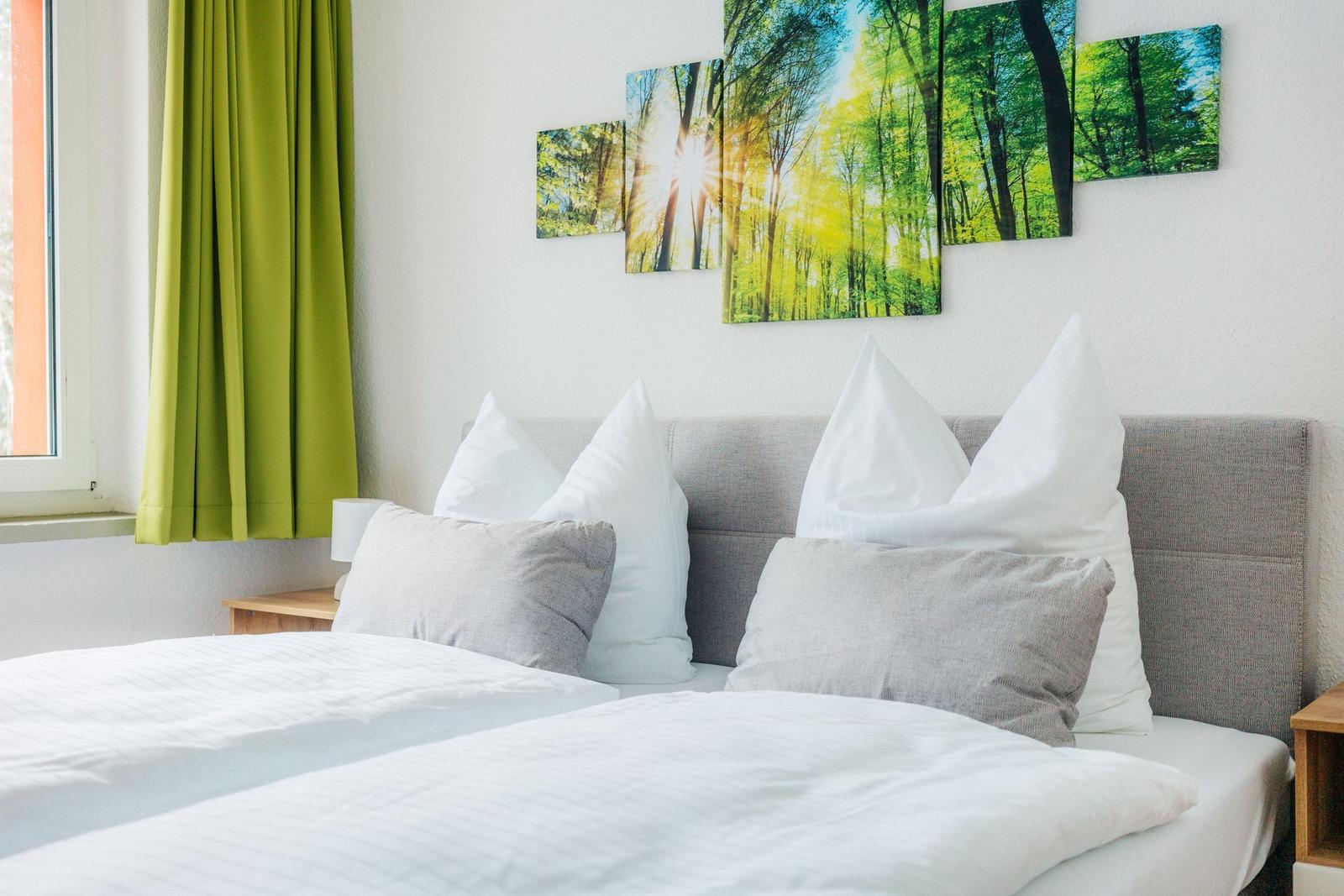 Schlafzimmer mit Bett, Kissen und Wandbild von Wald.