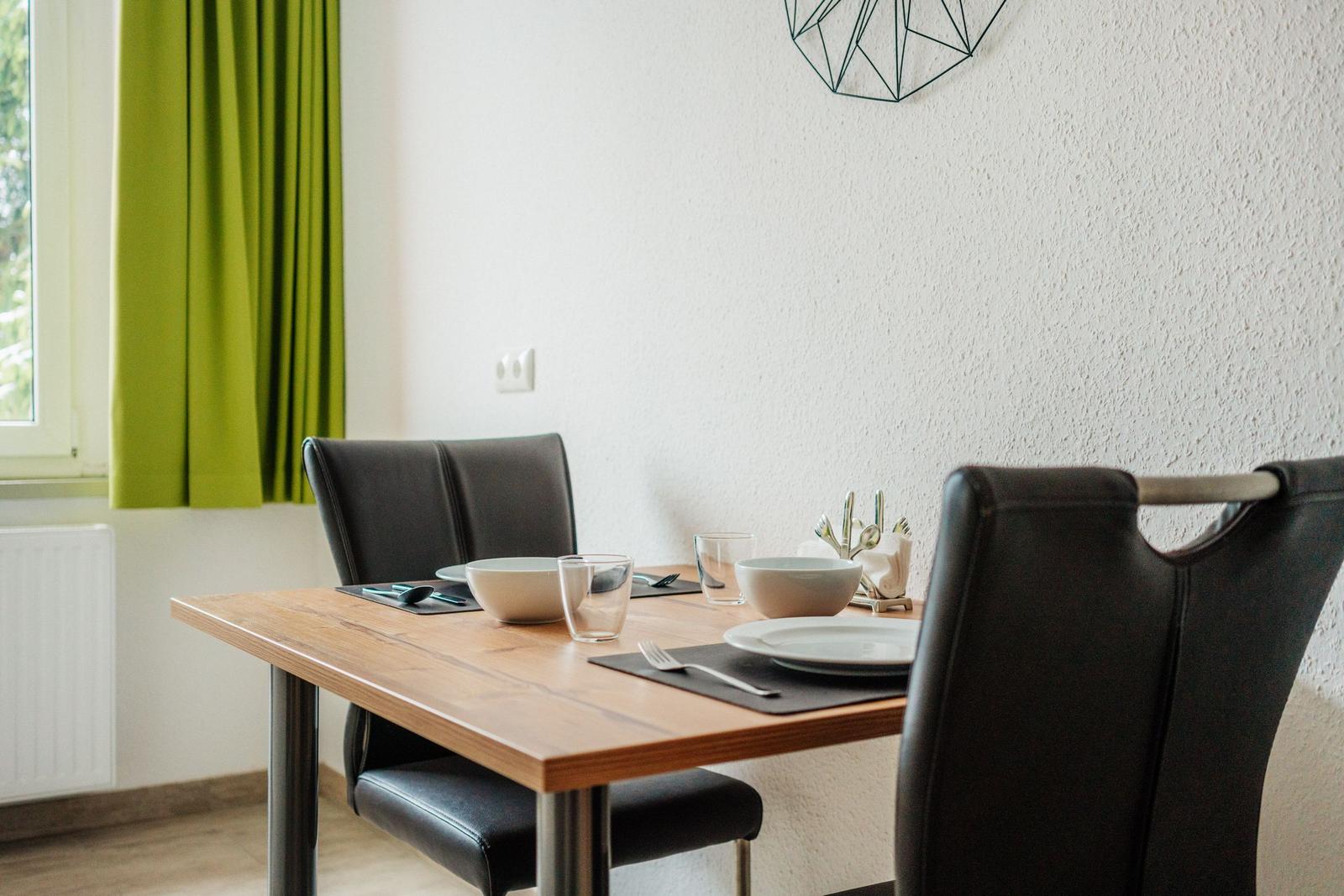 Esszimmer mit Holztisch, schwarzen Stühlen und grünen Vorhängen an Fenster