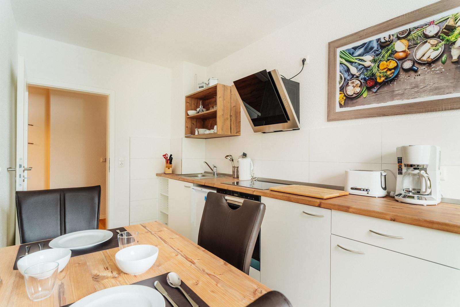 Küche mit Essbereich, Holztisch, weißen Schränken und Küchengeräten.