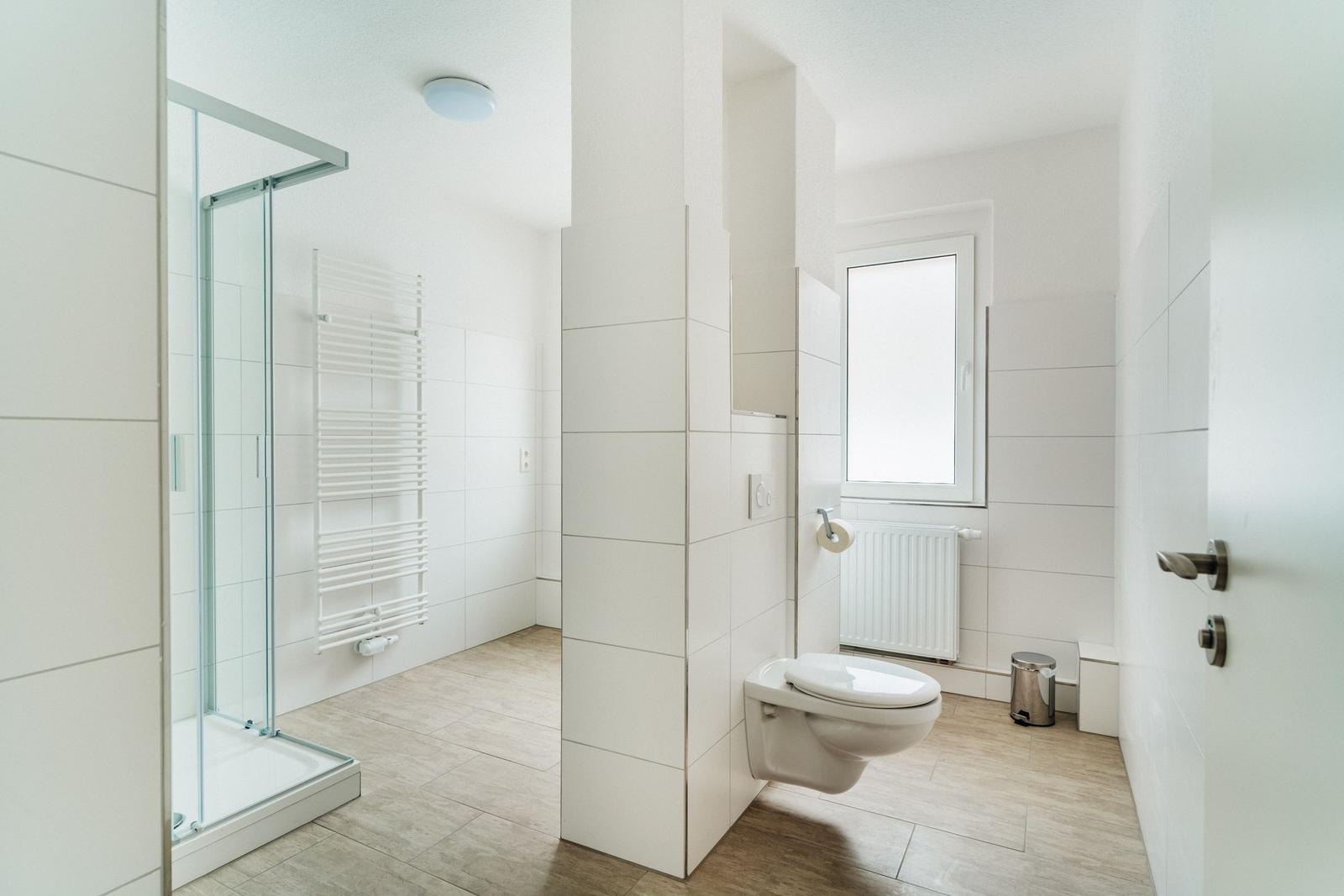 Badezimmer mit Dusche, Toilette und Fenster.