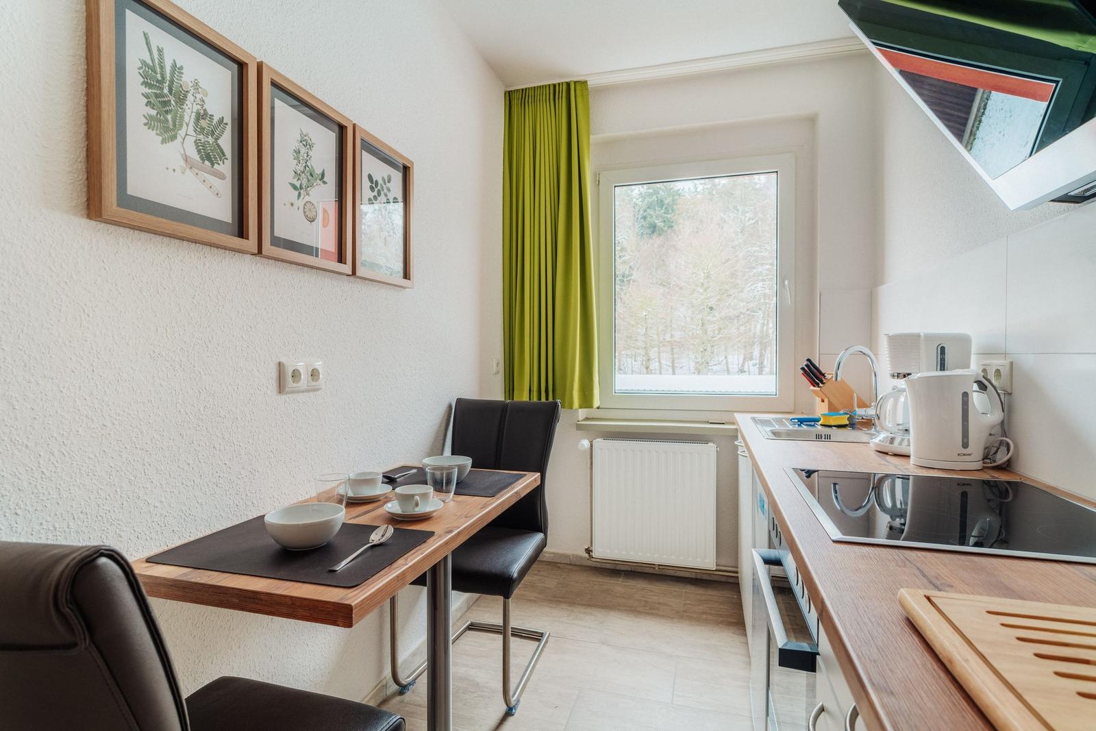 Küche mit Essbereich, Fenster mit grünen Vorhängen und Küchengeräten.