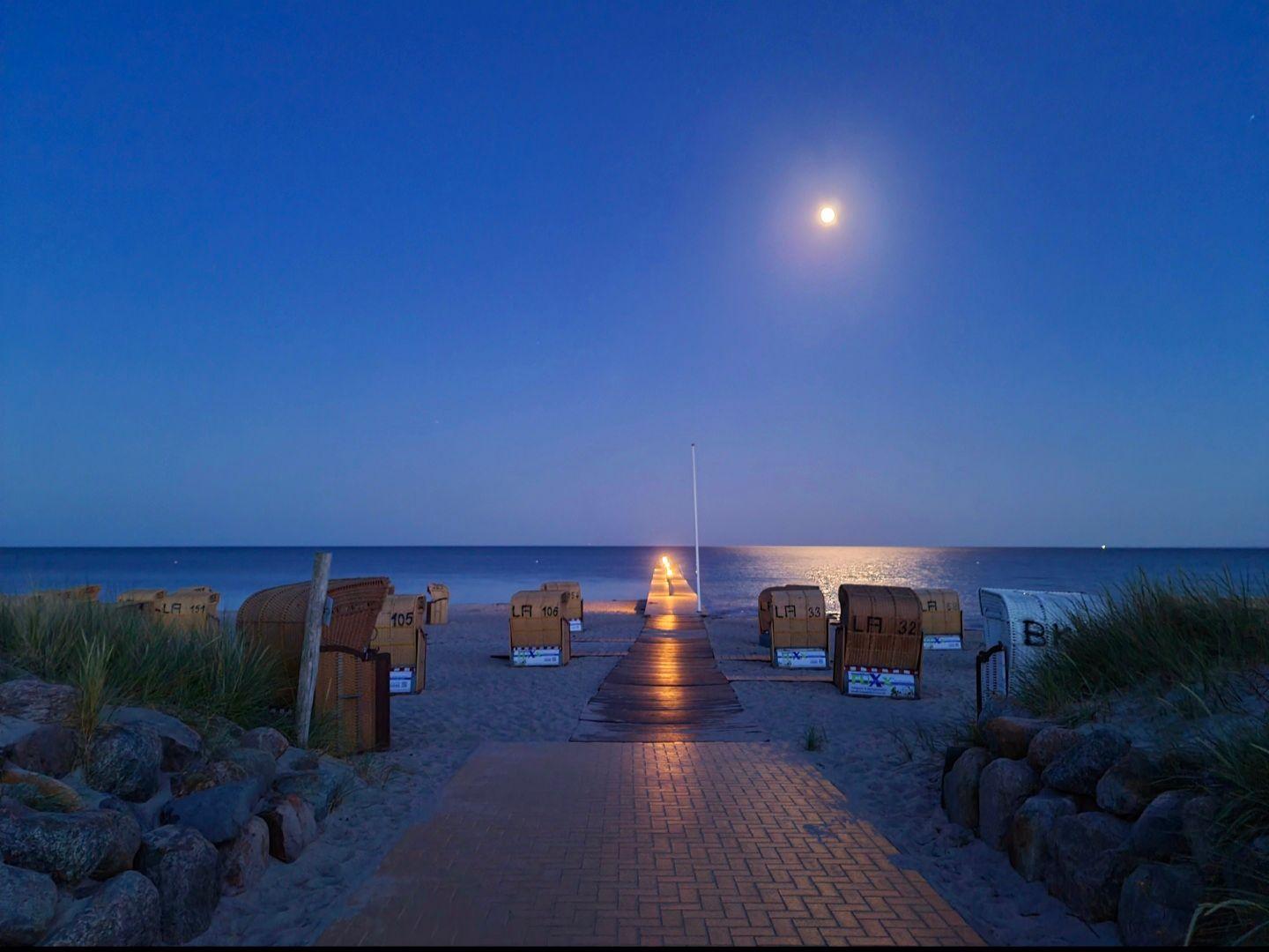 Stimmungsvolle Abendaufnahme am Südstrand mit Mondlicht, Strandkörben und beleuchtetem Weg zur Ostsee.