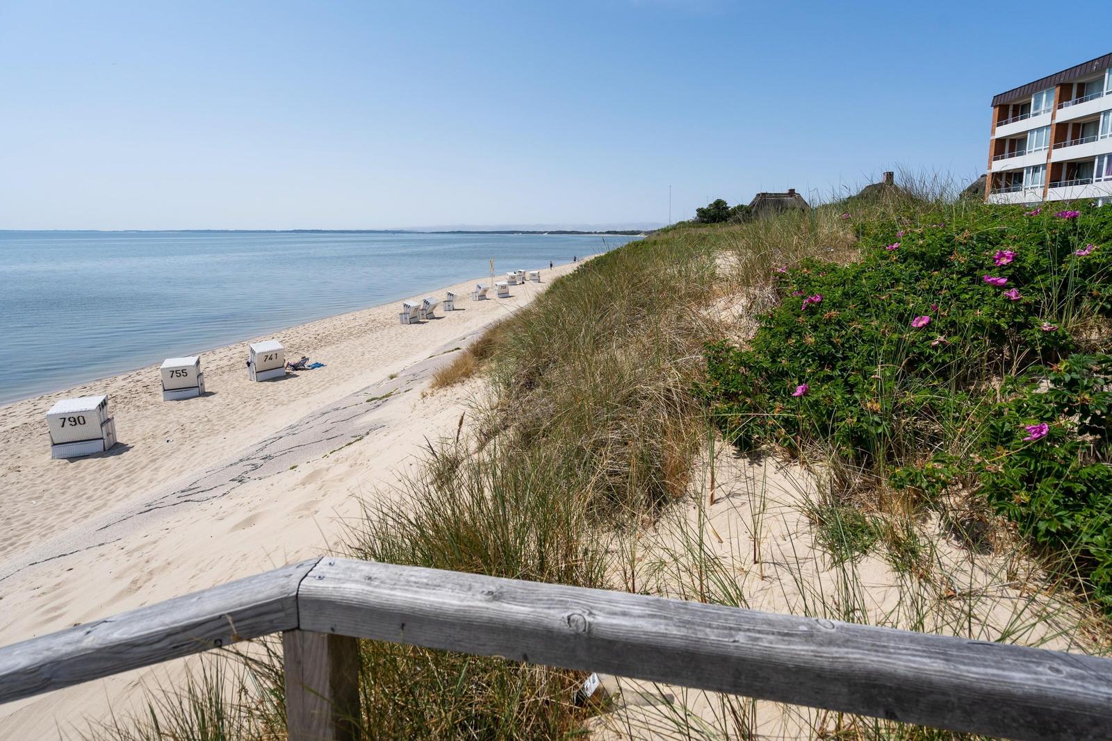 Strand mit Sand, Meer und Strandkörben. Im Hintergrund steht ein Gebäude.