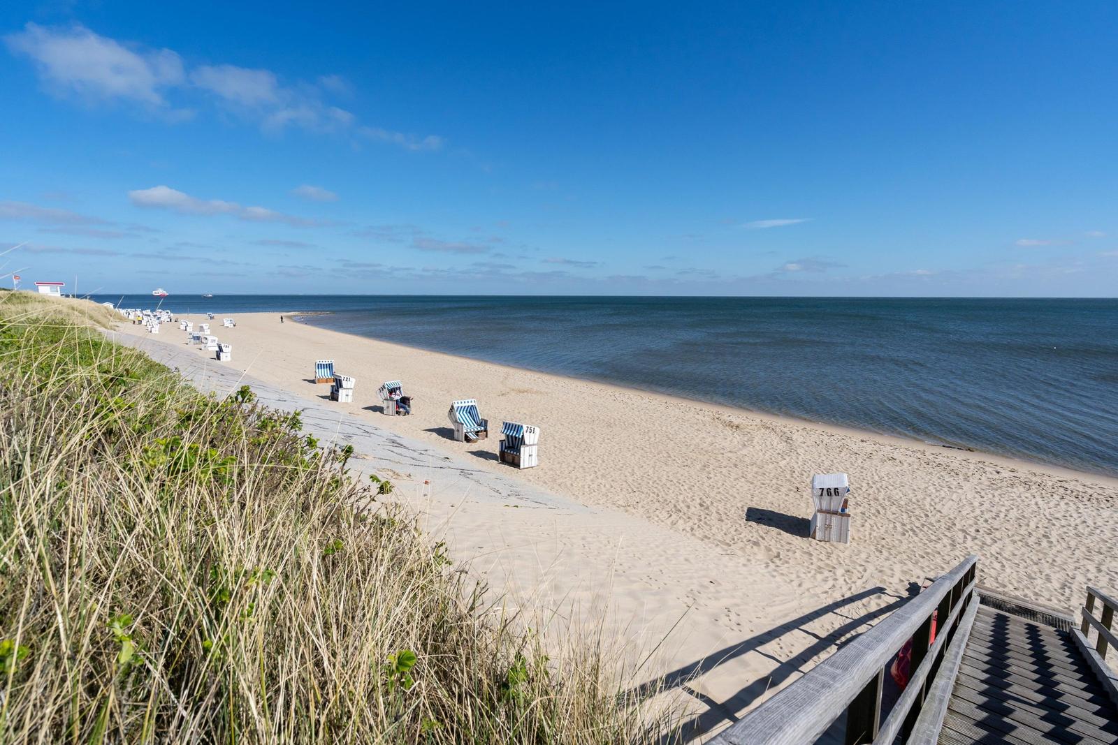 Strandkörbe mit blau-weißen Streifen stehen auf sandigem Strand.