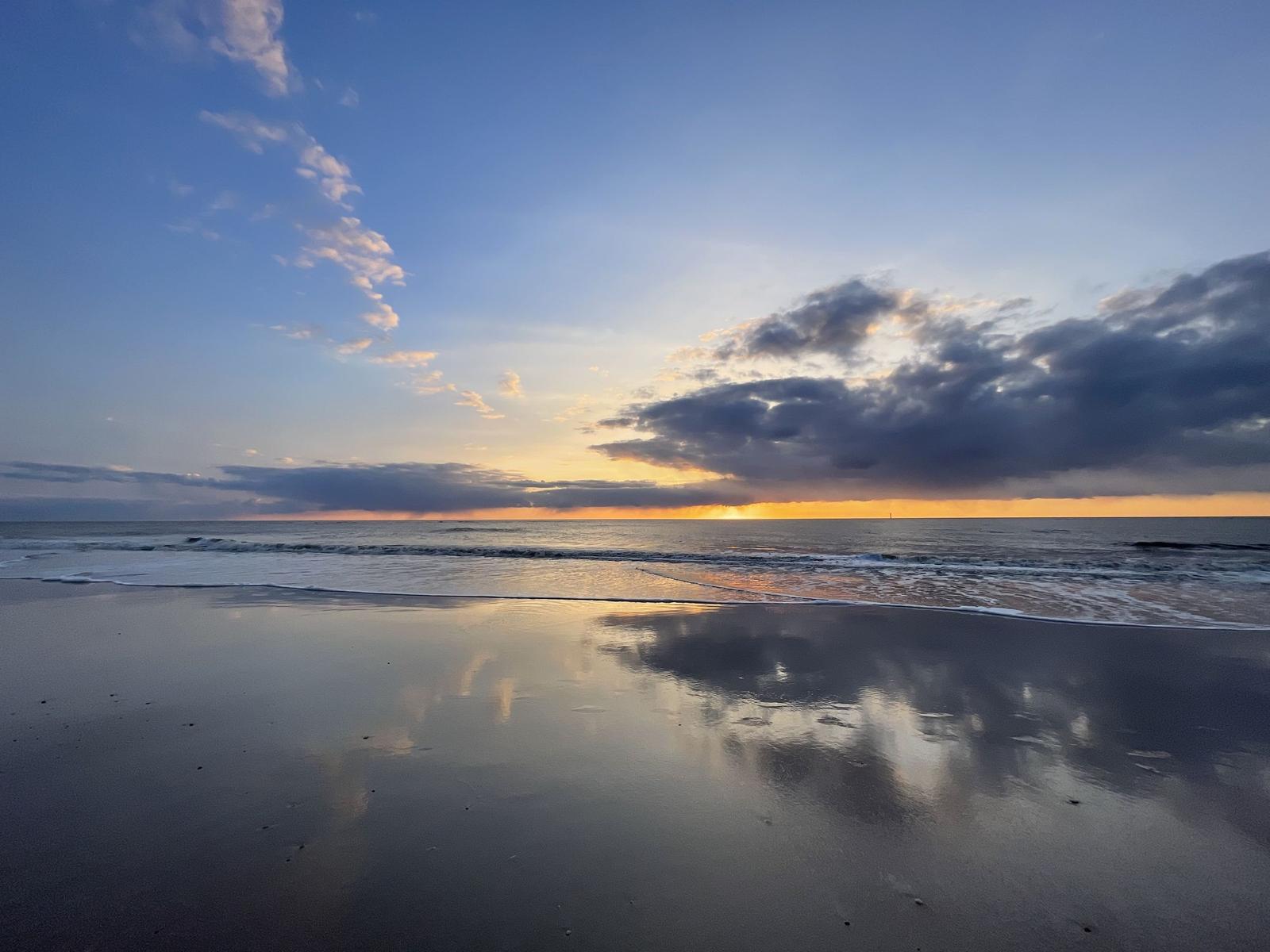 Strand mit Strandkörben und Holzsteg. Blick auf das Meer unter blauem Himmel.