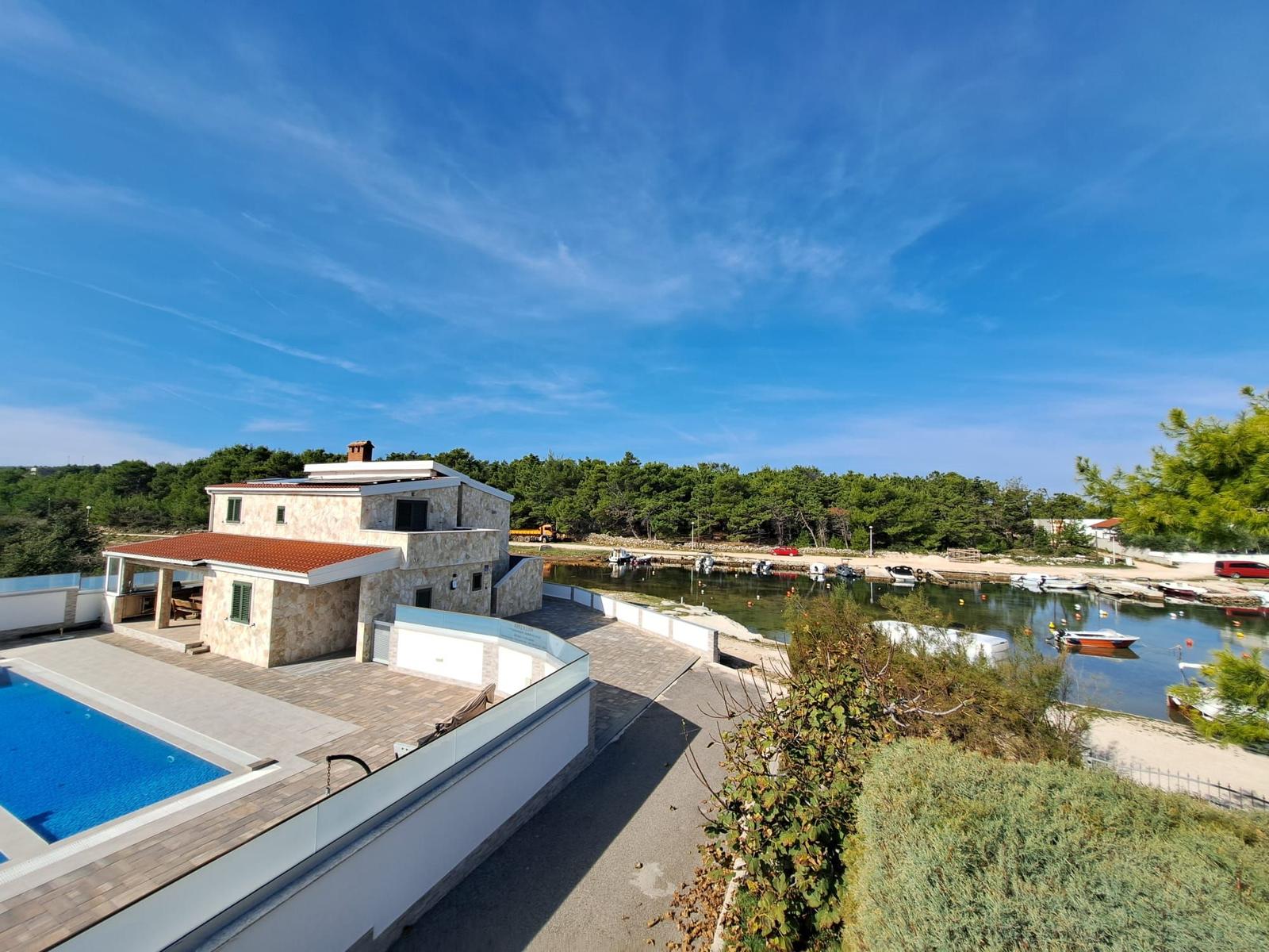 Villa mit Pool und Blick auf Hafen mit Booten und grüner Umgebung.