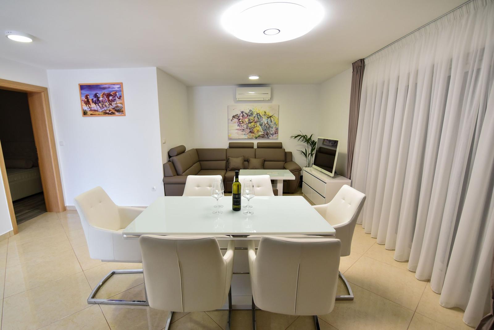 Essbereich mit weißem Tisch und Stühlen, dahinter Wohnbereich mit Sofa und Wandbildern.
