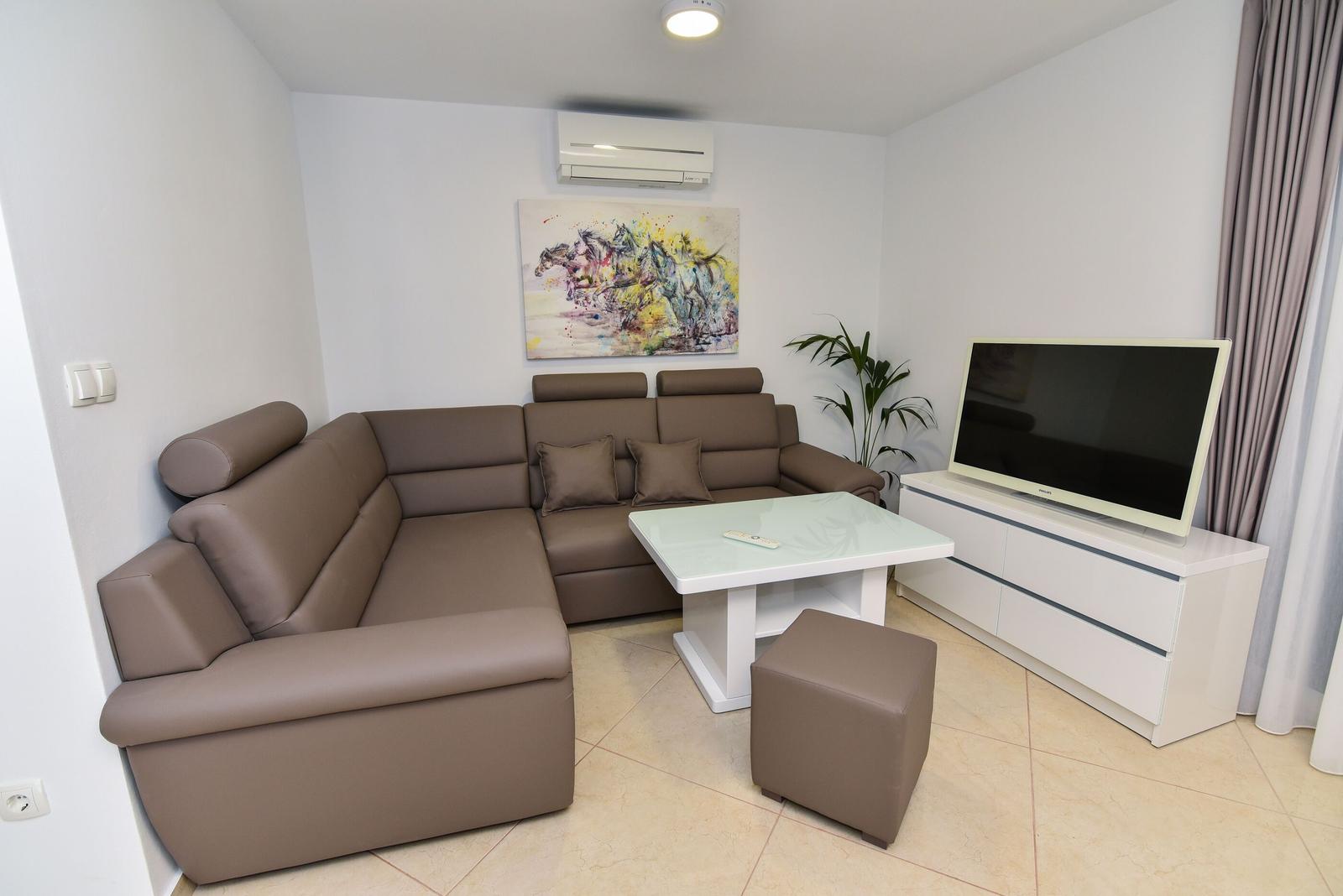 Wohnzimmer mit braunem Sofa, Fernseher und Glas-Tisch.