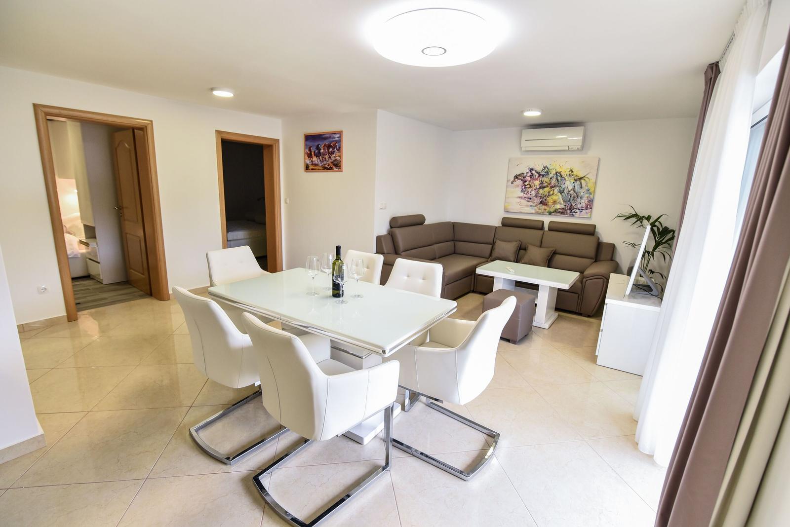 Essbereich mit weißem Tisch und Stühlen. Wohnbereich mit braunem Sofa und Wandbild.