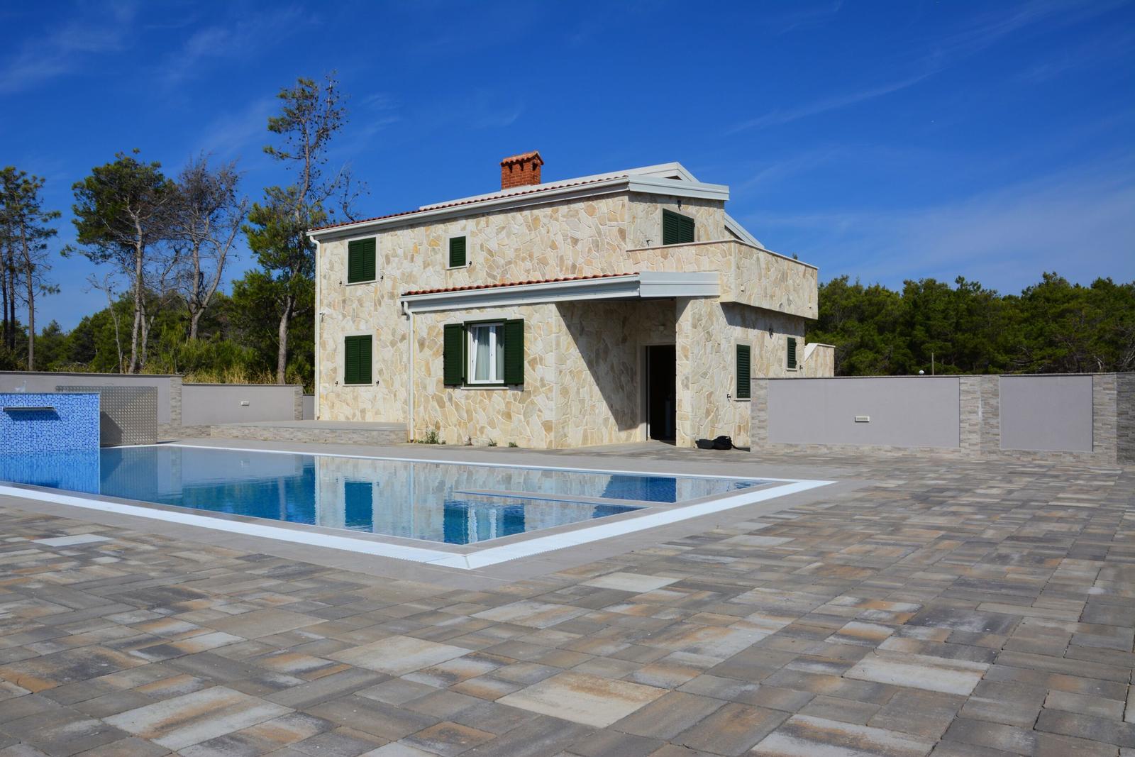 Steinhaus mit Pool und Terrasse unter blauem Himmel
