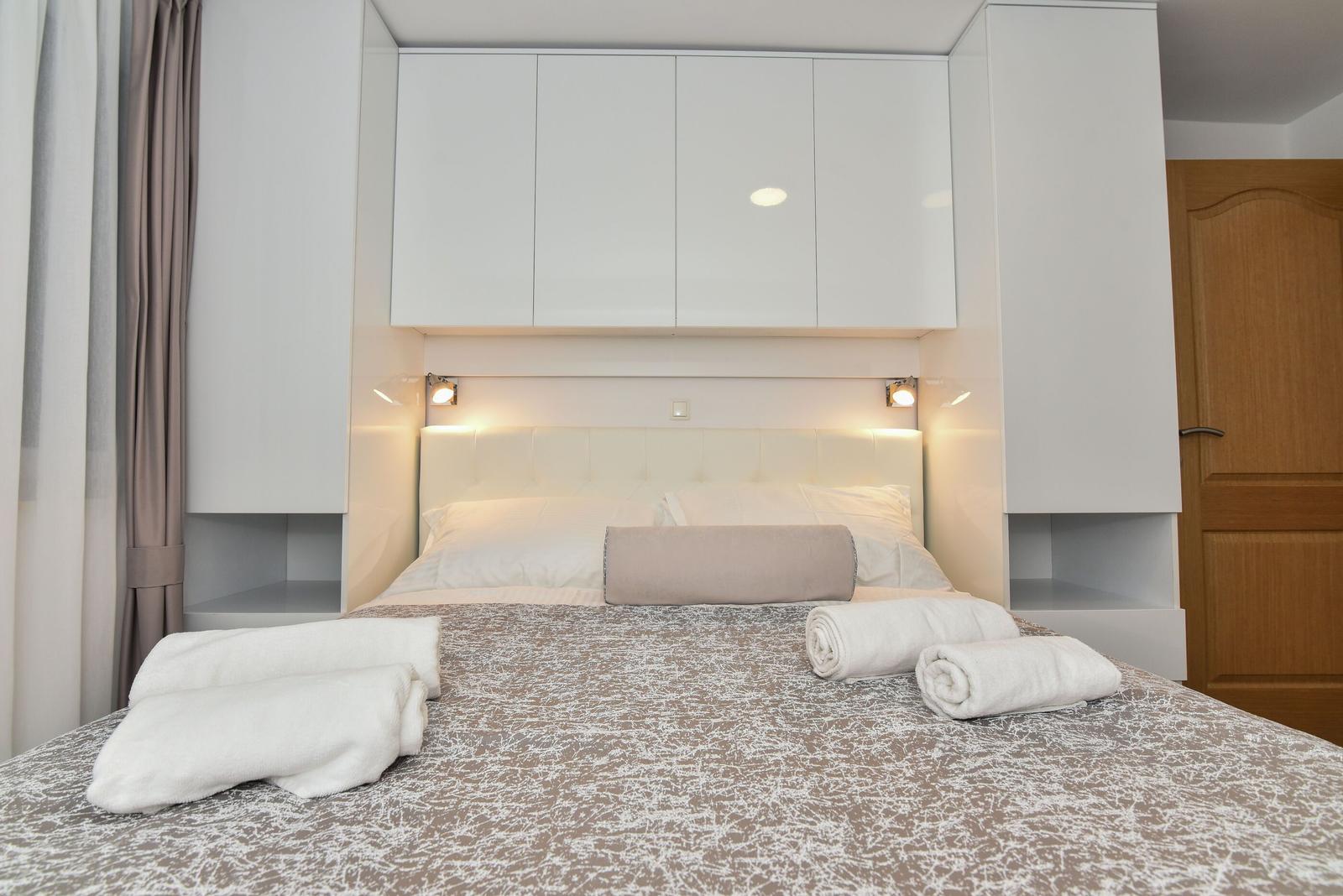 Schlafzimmer mit Bett, weißen Kabinen und aufgerollten Handtüchern.