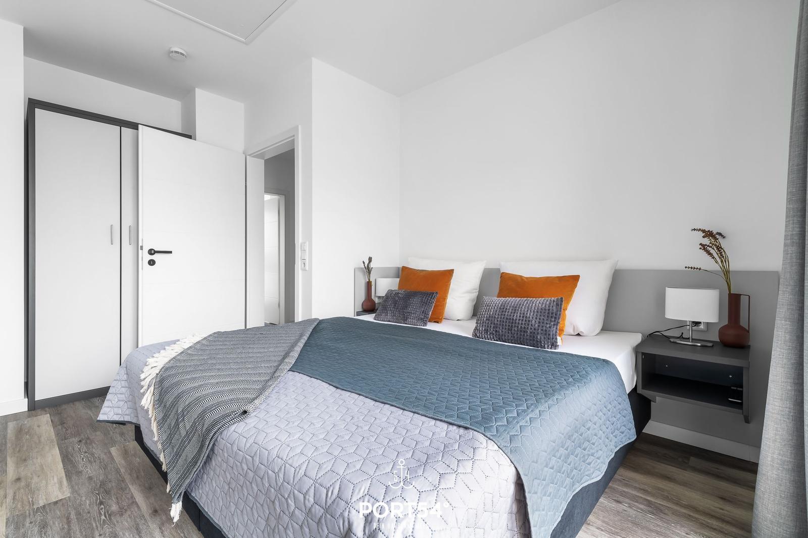Schlafzimmer mit Bett, Nachttisch und Kleiderschrank. Boden aus Holz.