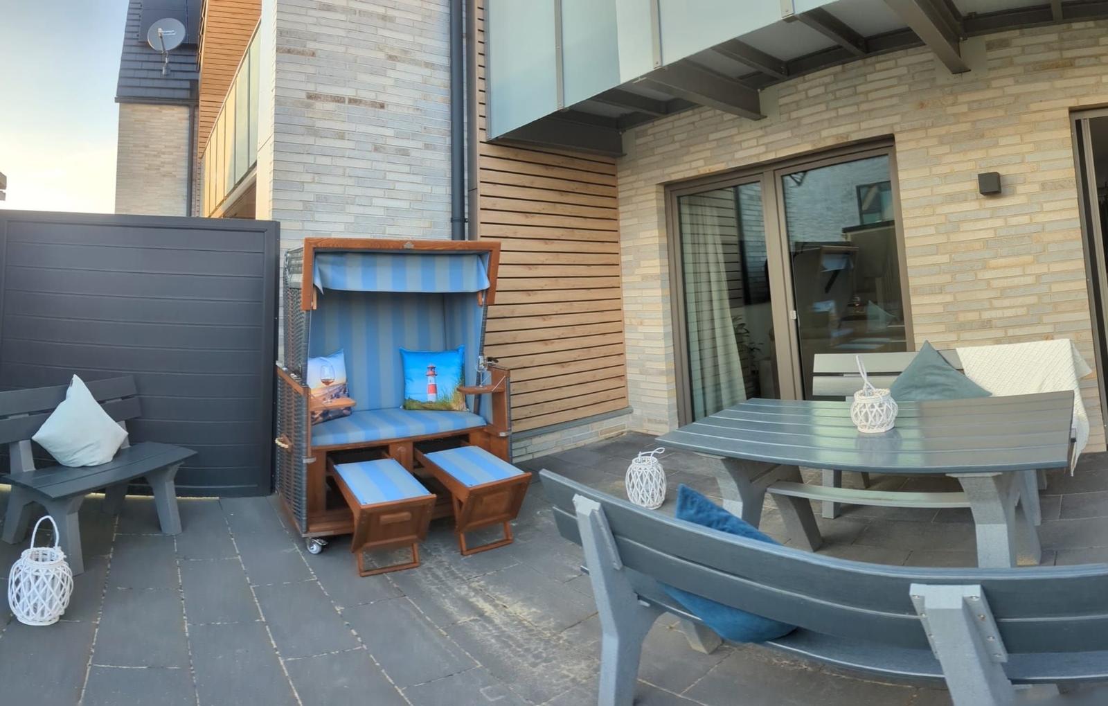 Terrasse mit Strandkorb, Tisch und Bänken. Modernes Haus mit Holz- und Steinverkleidung.