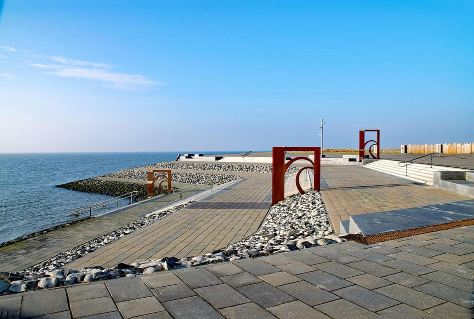 Steinpflasterweg mit roten Metallstrukturen am Strand. Blick auf das Meer unter blauem Himmel.