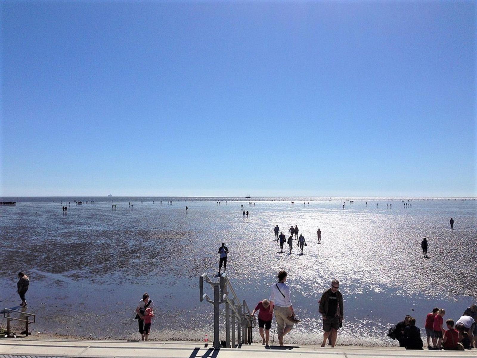 Menschen spazieren am Strand bei sonnigem Wetter mit klarem Himmel und Wasser.