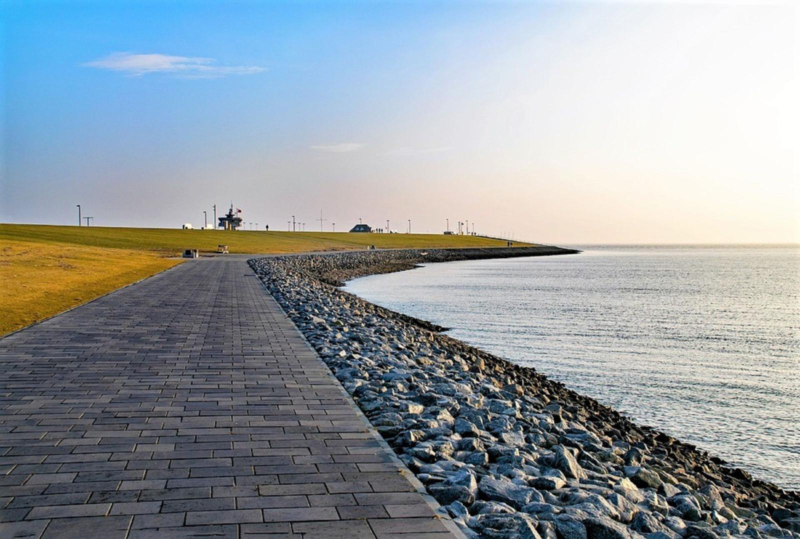 Pfad entlang steiniger Küste mit Blick auf ruhiges Wasser und grasbewachsenen Hang.
