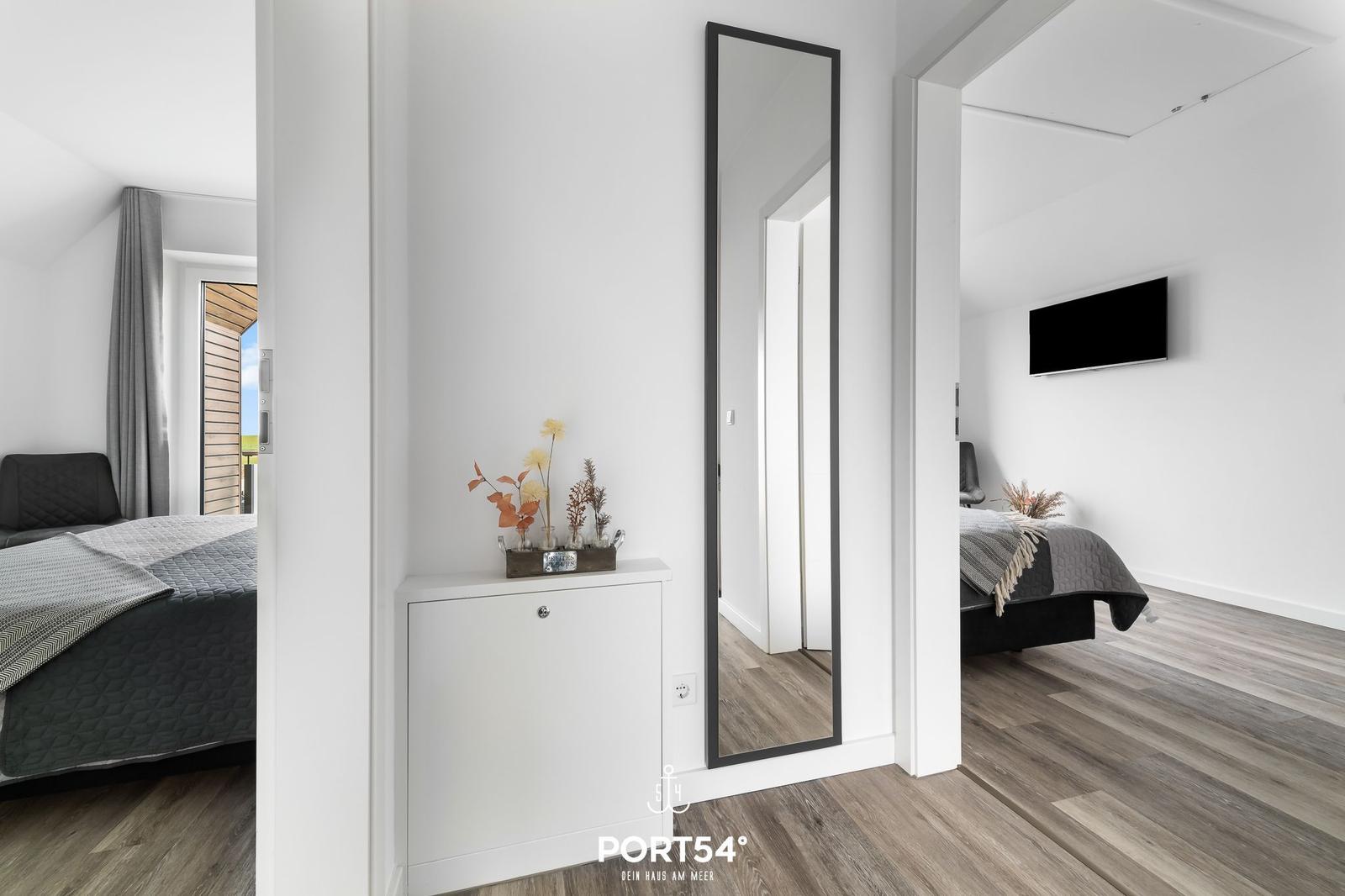 Zimmer mit Spiegel, Kleiderschrank und Bett. Holzboden und Wand-TV sichtbar.