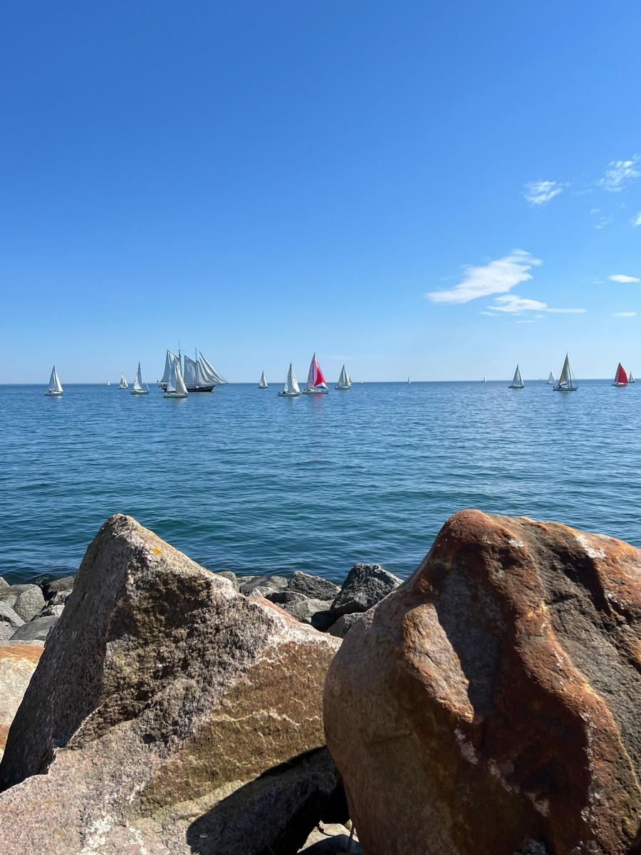Sailboats auf dem Wasser, große Felsen im Vordergrund, klarer blauer Himmel.