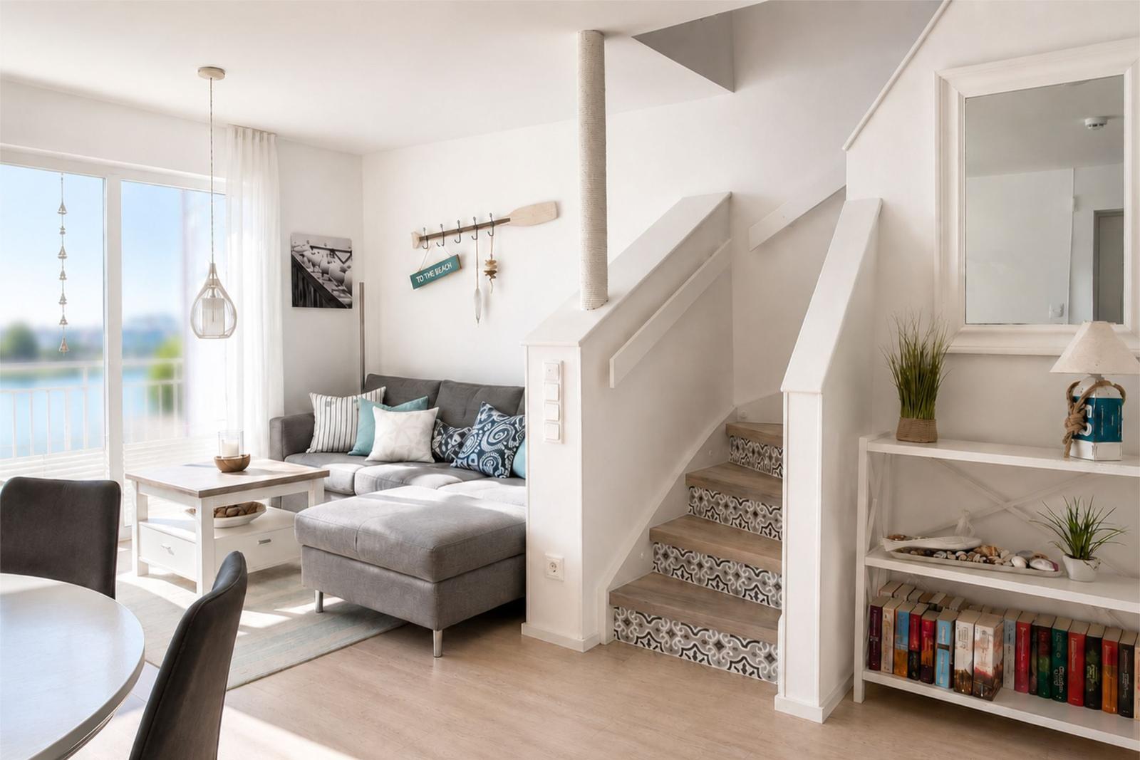 Wohnzimmer mit Sofa, Treppe und Bücherregal. Blick auf den Balkon.
