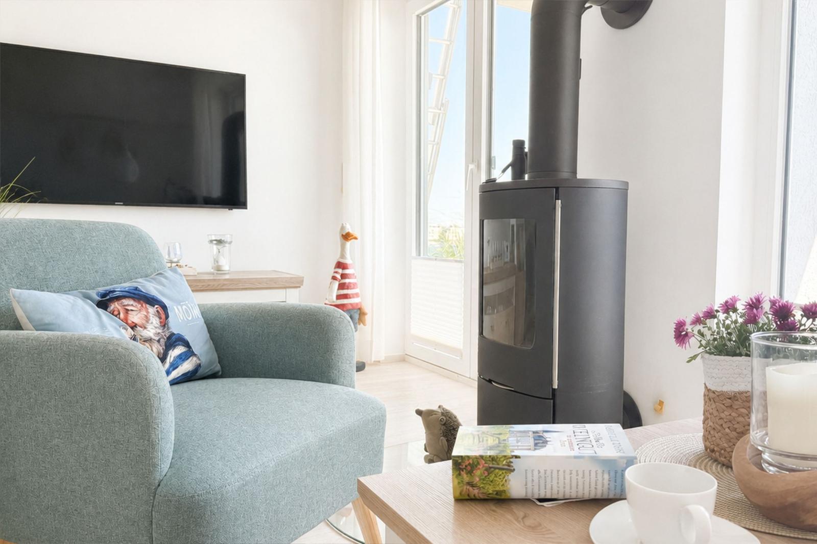 Ein Wohnzimmer mit Sofa, Kaminofen und Fernseher. Auf dem Tisch steht eine Tasse und ein Buch.