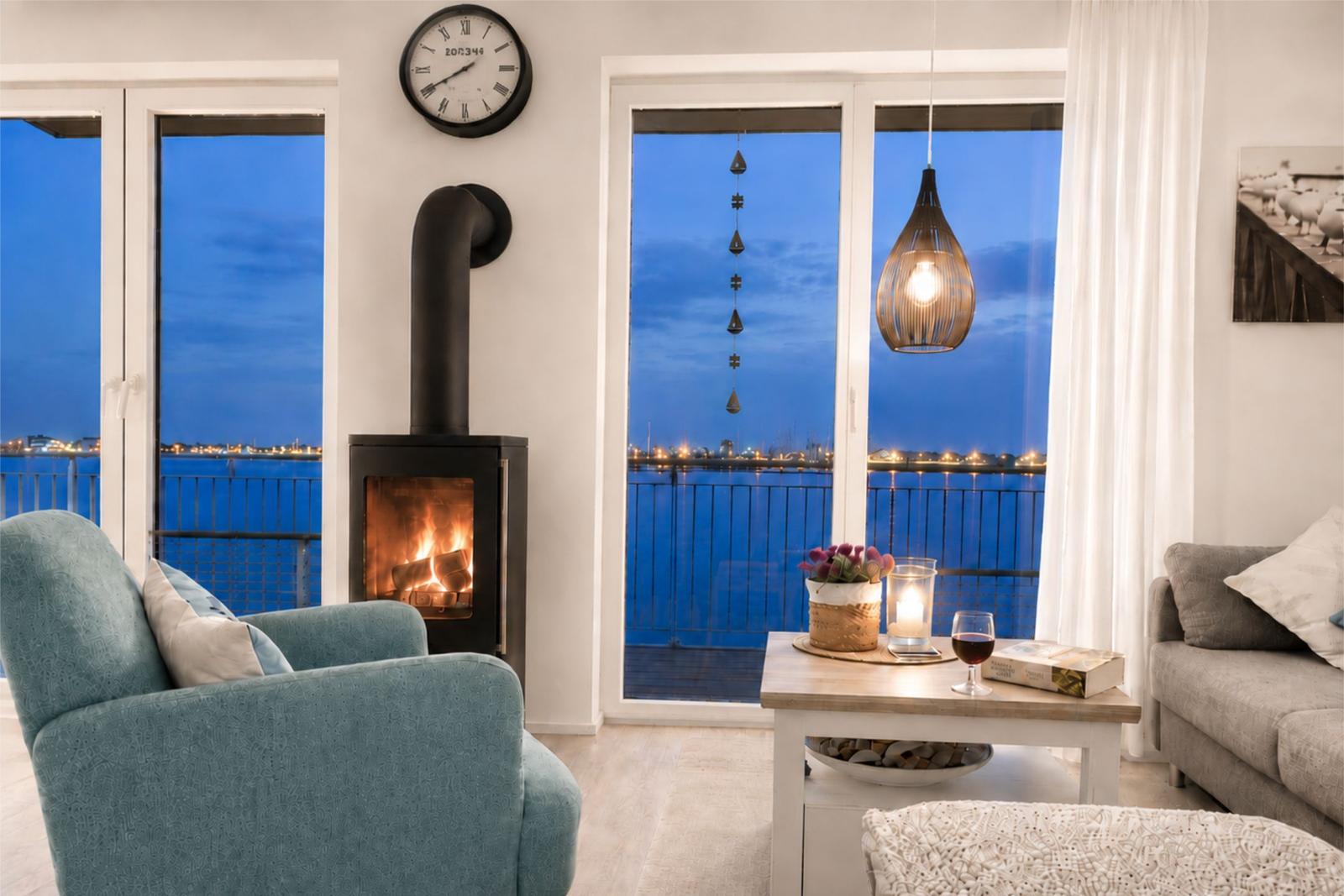 Wohnzimmer mit Kamin, Balkon und Blick auf Wasser.