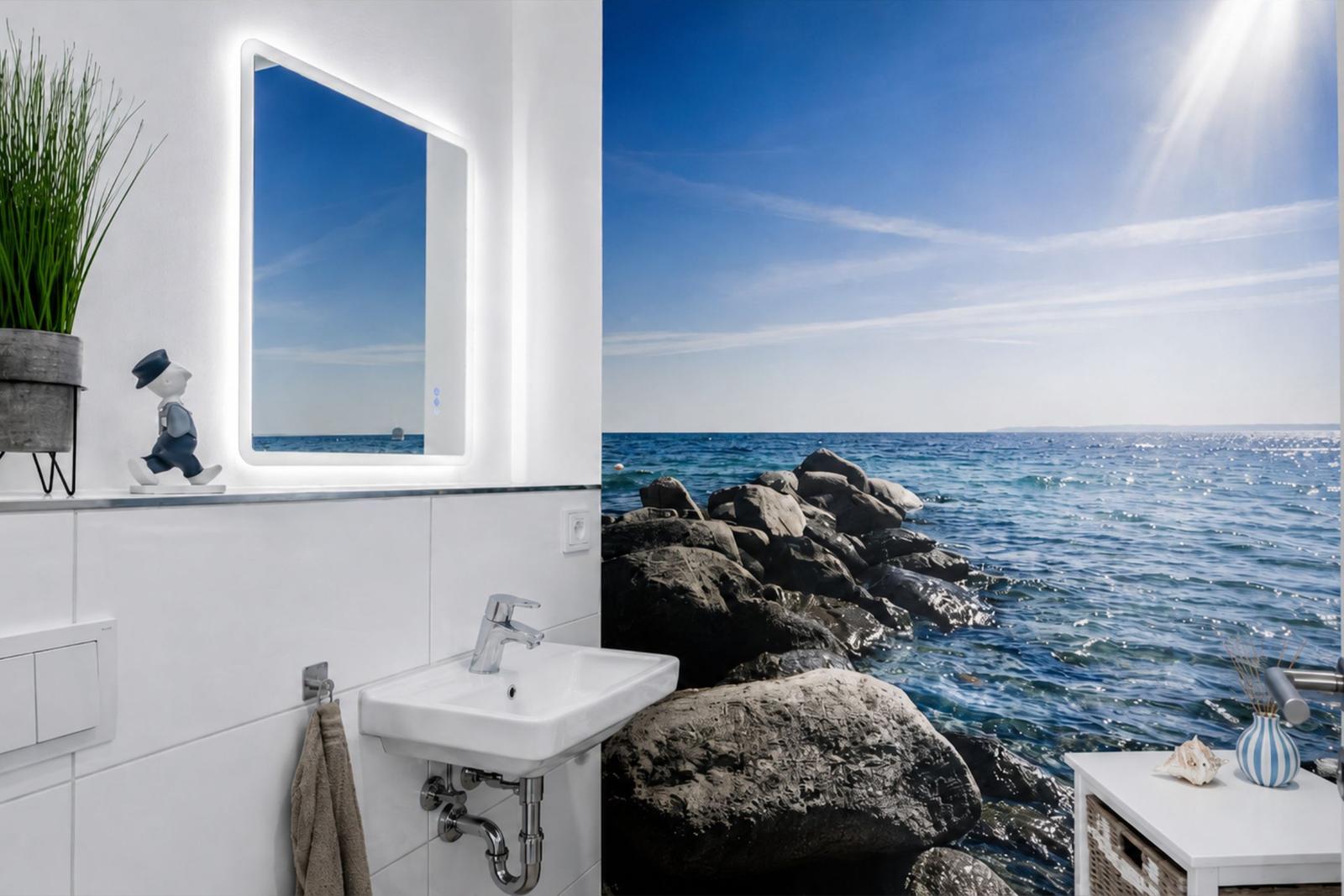 Badezimmer mit Meeresmotiv-Wand, Waschbecken und beleuchtetem Spiegel.