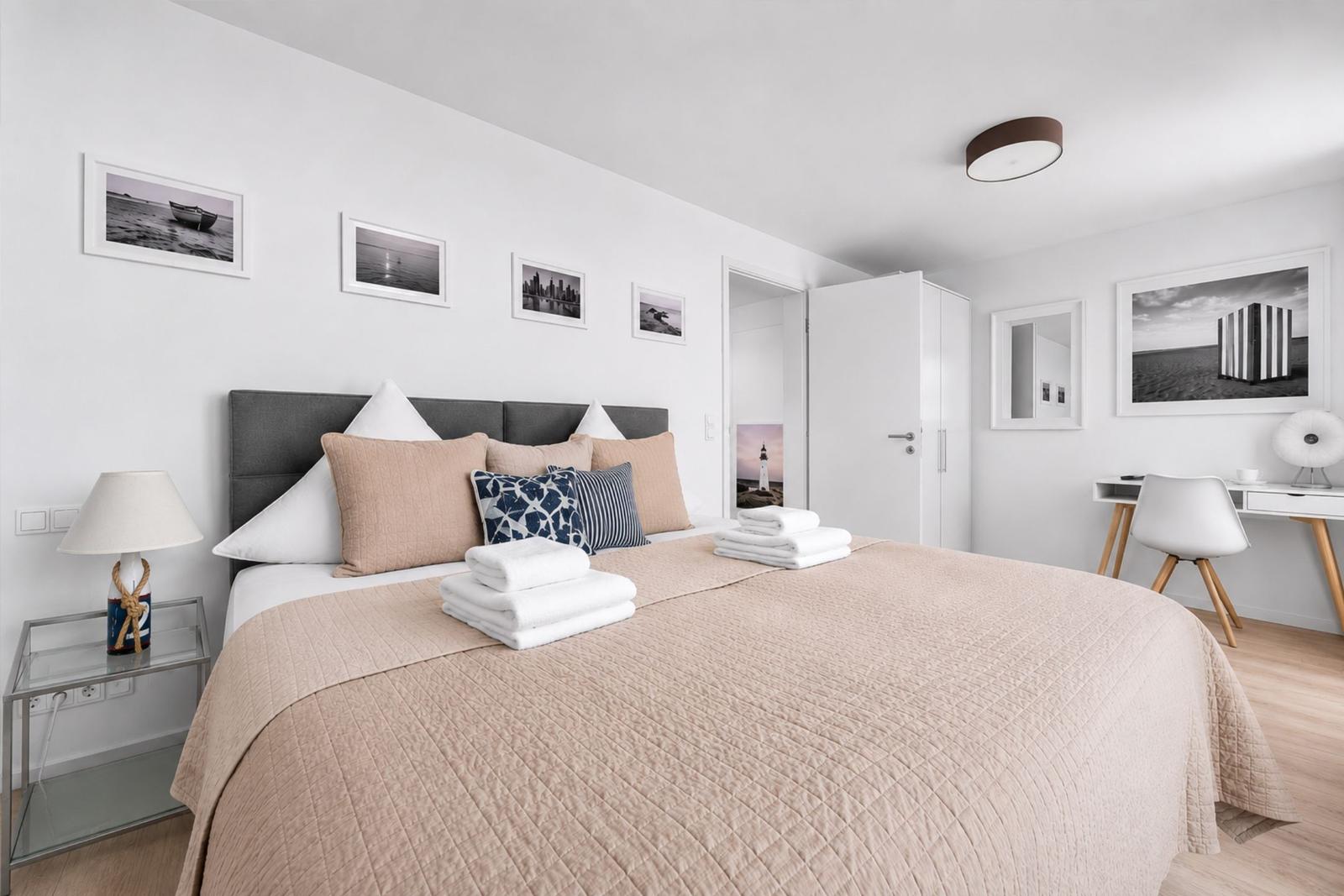 Schlafzimmer mit Bett, Nachttisch, Schreibtisch und Wandbildern.