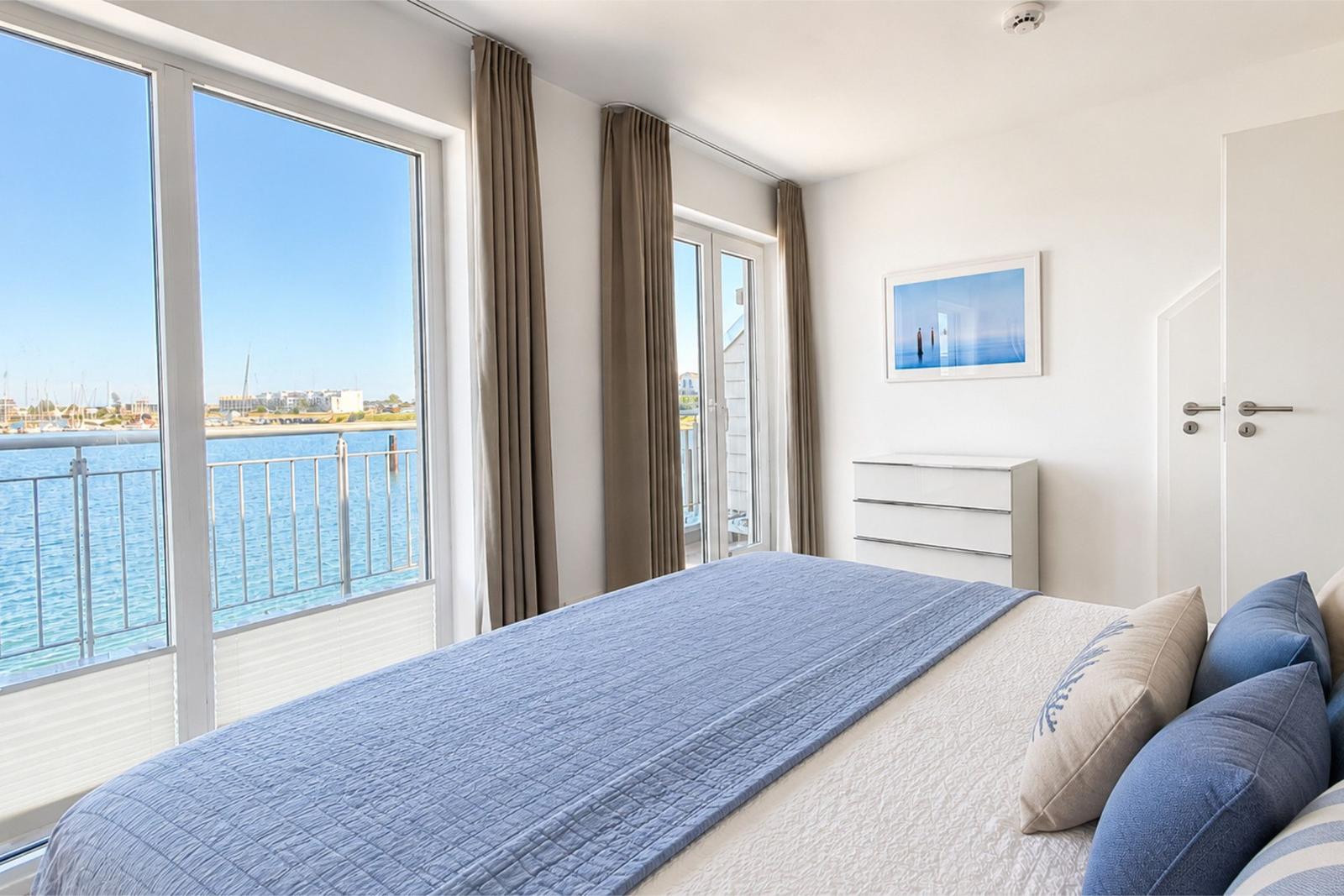Schlafzimmer mit Blick auf Hafen und Wasser, großes Bett, Fenster und Tür zum Balkon.
