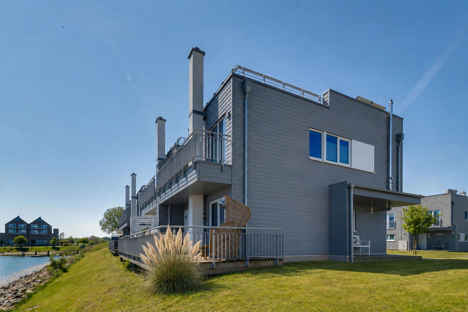 Moderne Villa mit Balkon, Garten und Blick auf Wasser.