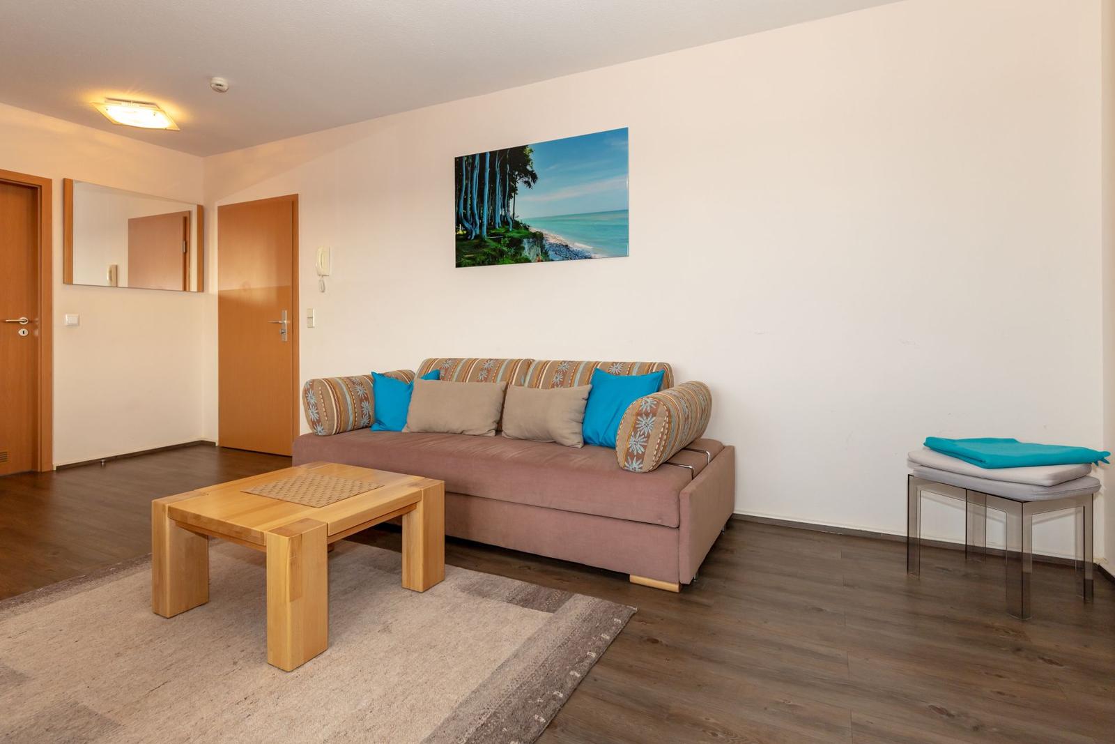 Living room with sofa, table, and wall art. Wooden floor and light walls.