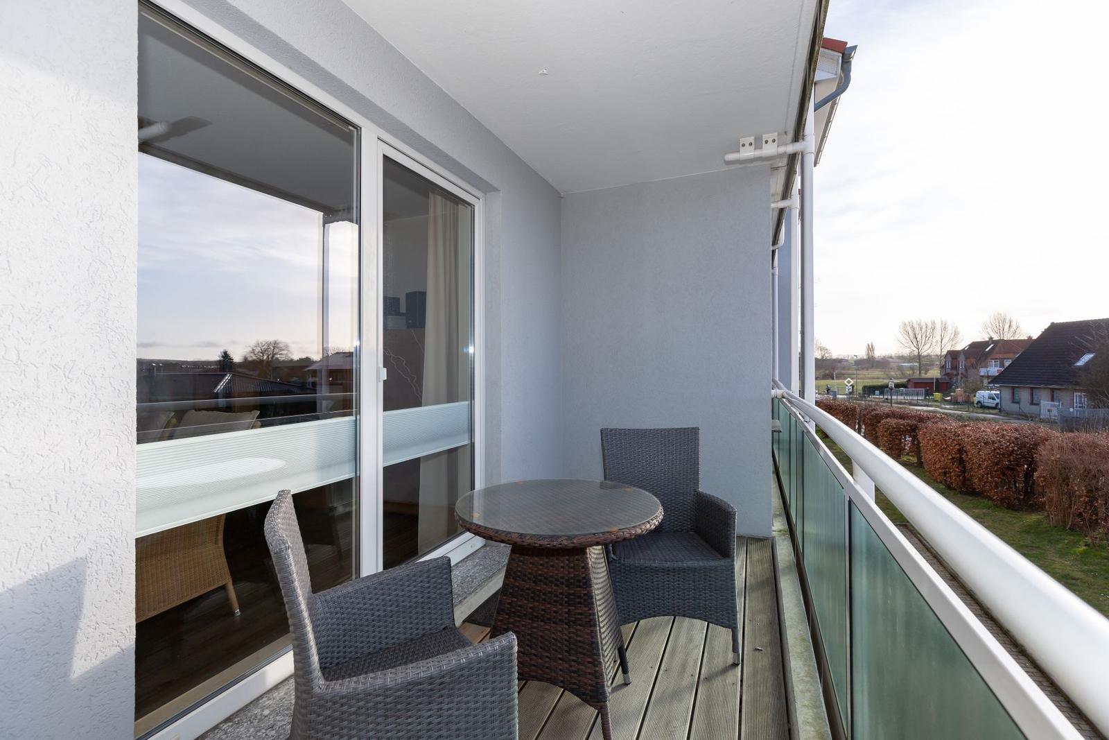 Balcony with table and two chairs, glass railing, view of residential area.