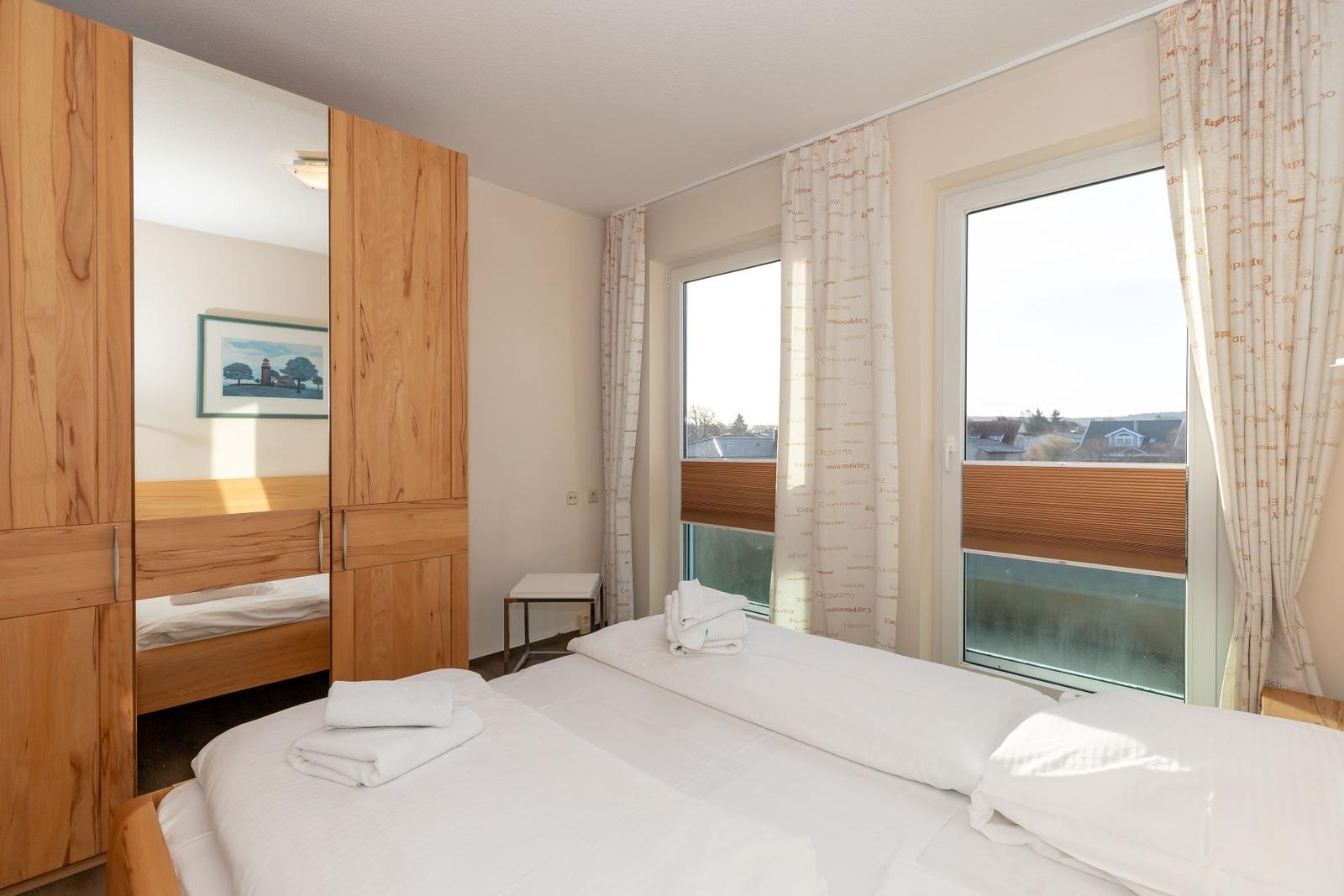 Bedroom with double bed, wooden wardrobe, and window view.