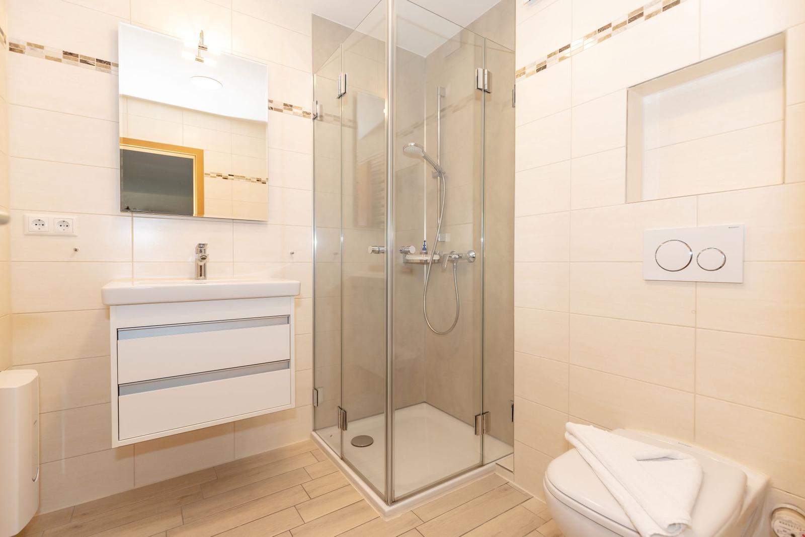 Bathroom with shower, sink, and toilet. Tiled wall and wooden floor.