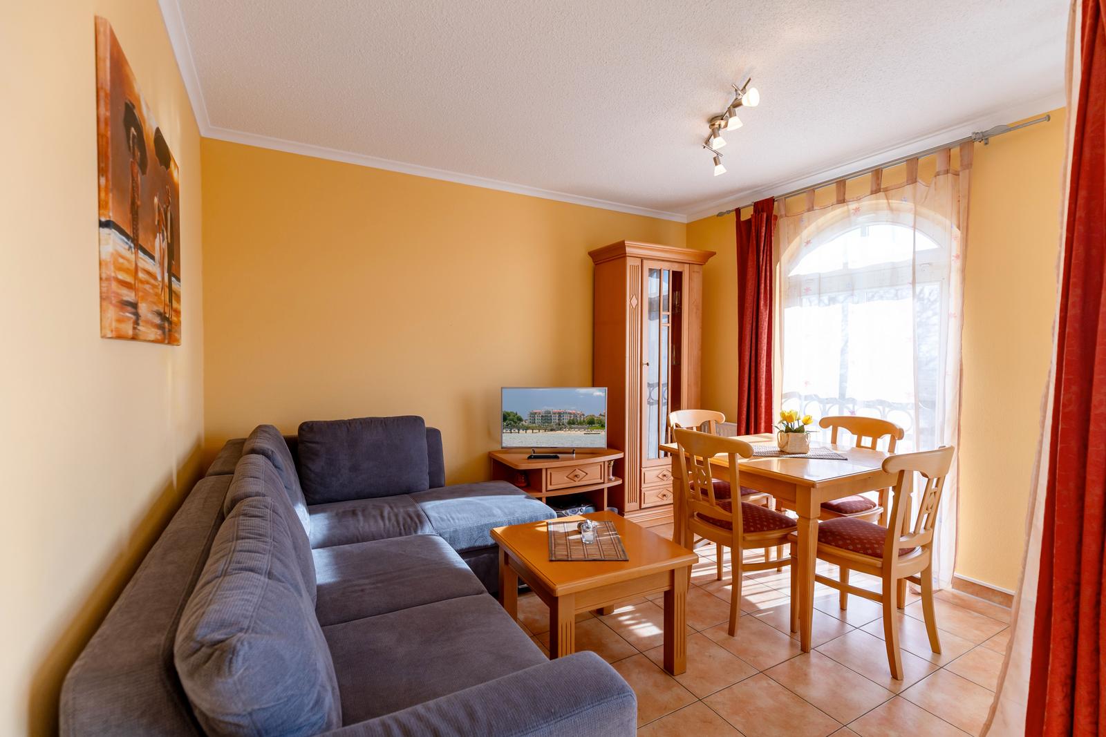 Wohn- und Essbereich mit Sofa, Esstisch und Fernseher. Gelbe Wände und Holzmöbel.