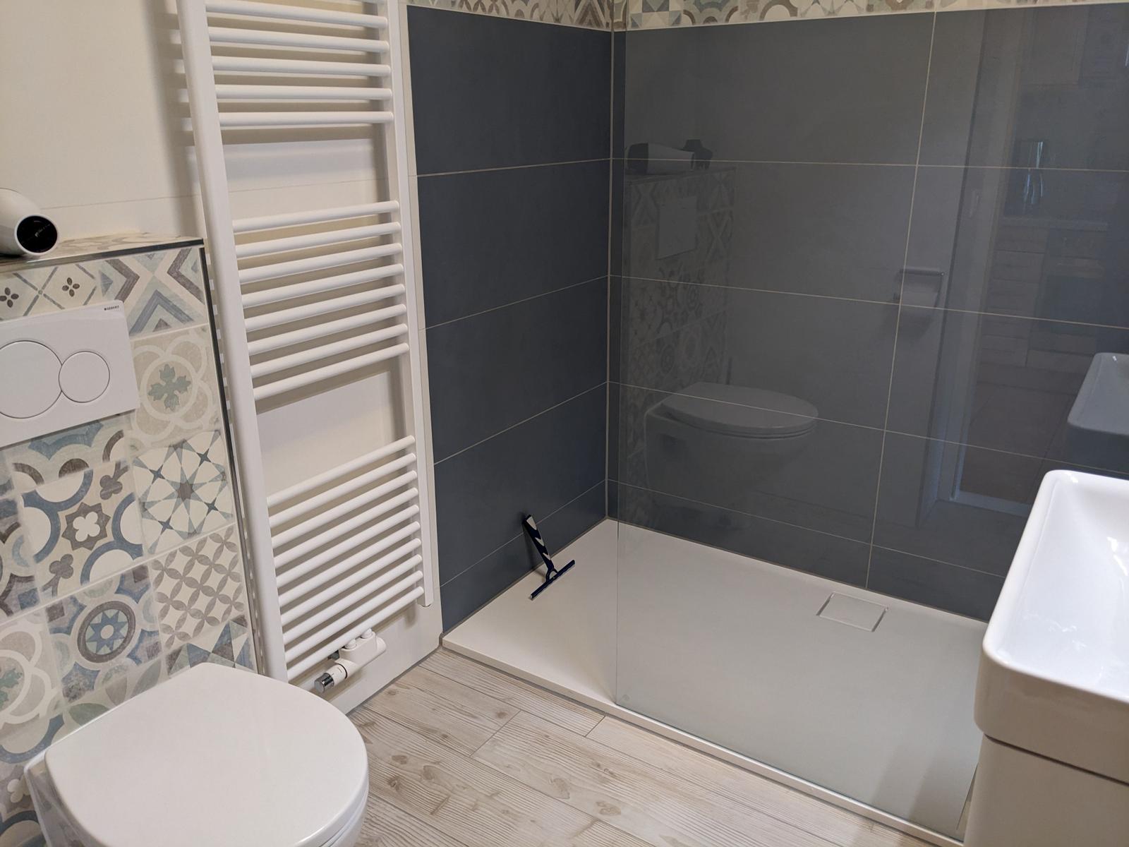 Badezimmer mit Dusche, Toilette und Waschbecken. Wandfliesen mit Muster und Holzdielen.