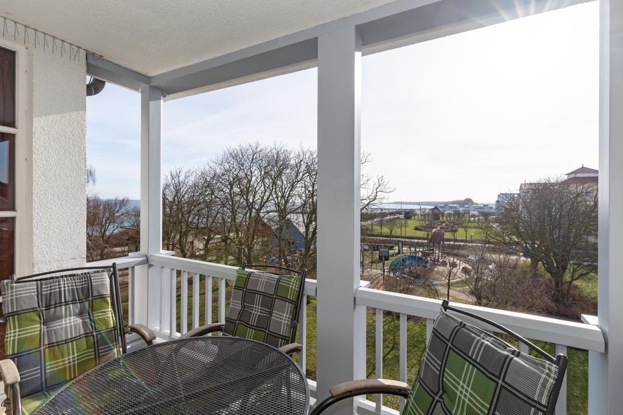 Terrasse mit Tisch und drei Stühlen, Blick auf Grünfläche und Gebäude.