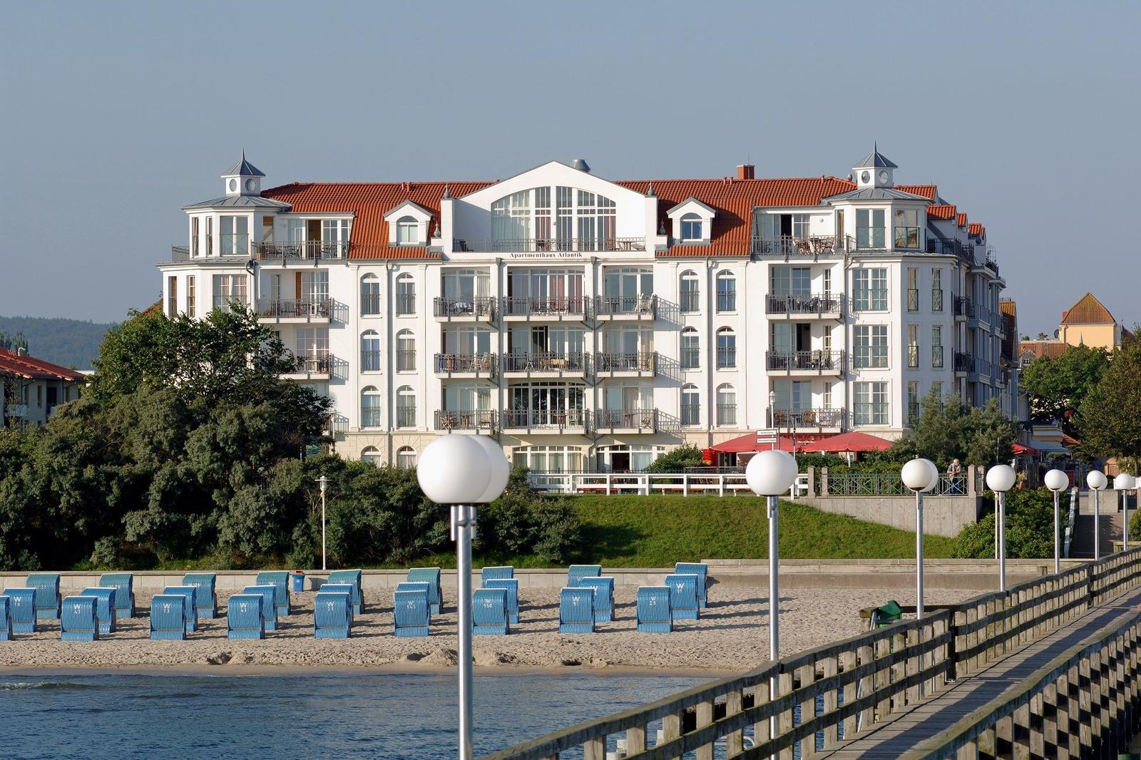Wohnhaus mit Balkonen und rotem Dach an Strand mit Strandkörben.