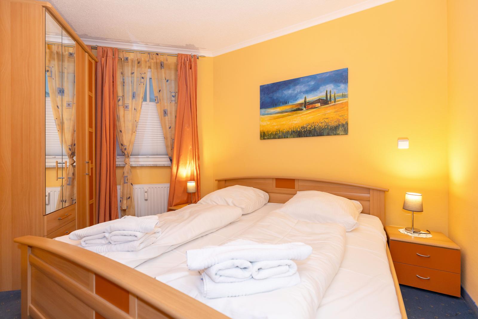 Schlafzimmer mit Doppelbett, Nachttisch, Gardinen und Wandbild.