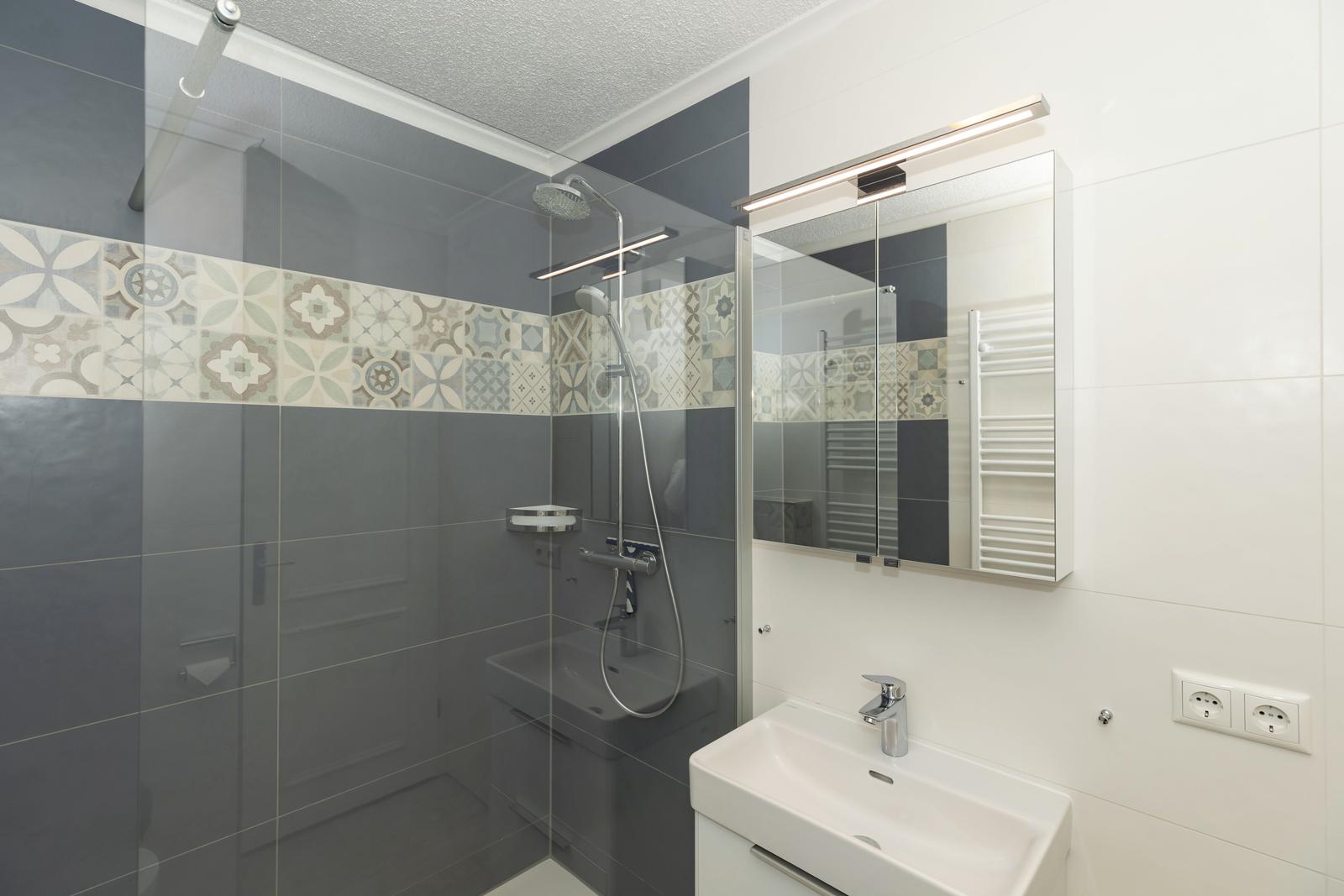 Bad mit Dusche, Spiegel und Waschbecken.