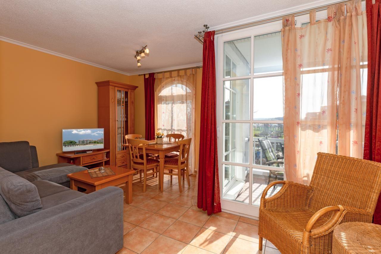 Wohn- und Essbereich mit Sofa, Esstisch und Balkon. Rote Vorhänge und Holzmöbel.