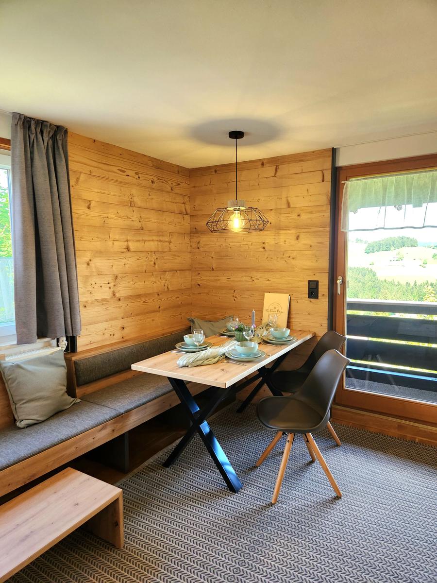 Essbereich mit Holzwand, Tisch, Stühlen und Blick auf Balkon.