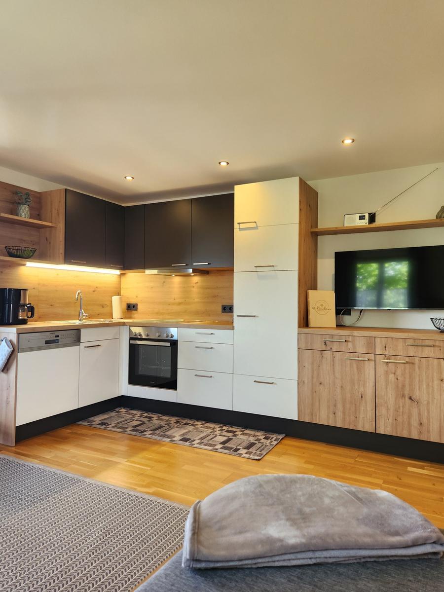 Küche mit Holz- und weißen Schränken, Spüle, Herd und Fernseher
