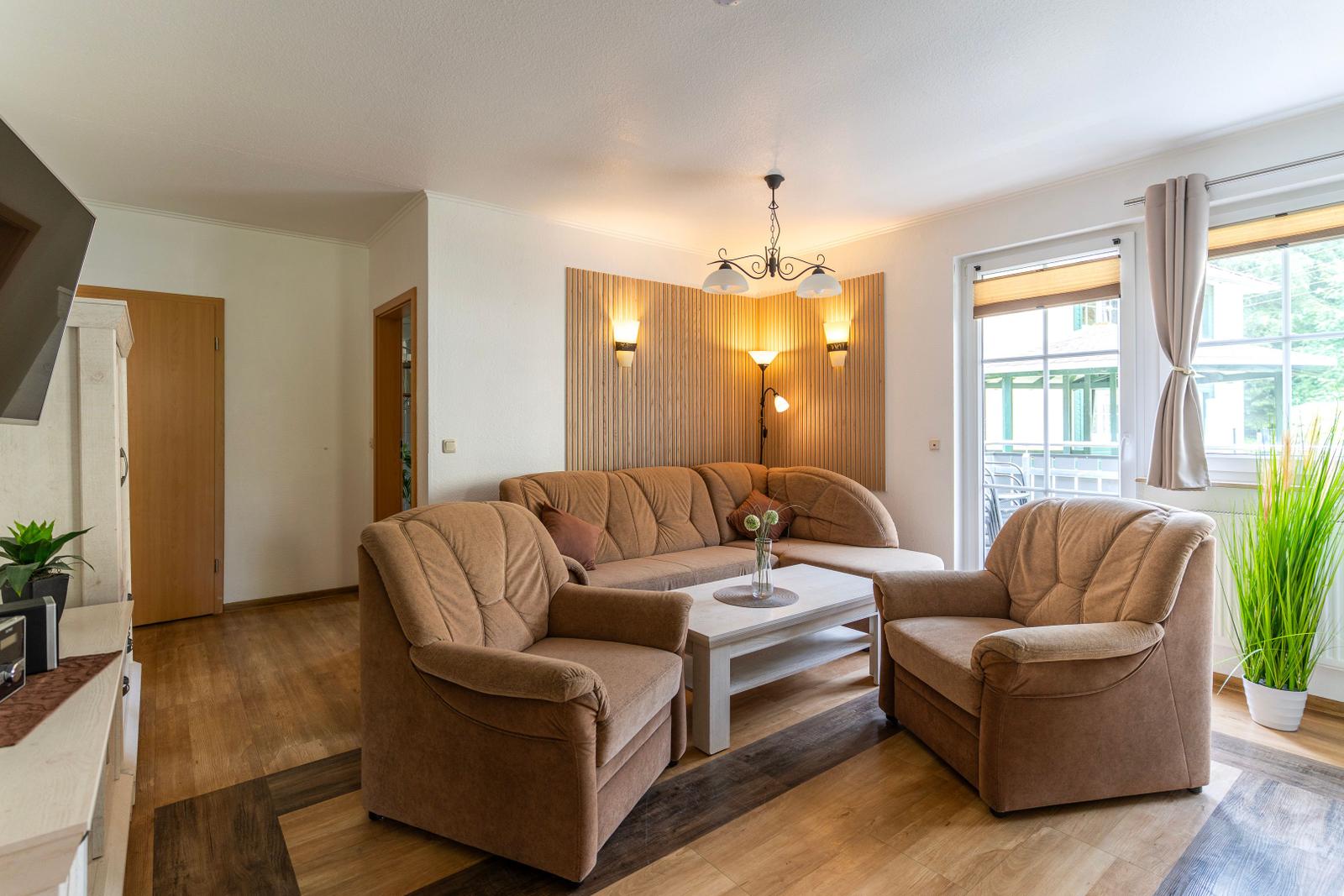 Wohnzimmer mit braunen Sesseln, Sofa und weißem Tisch. Holzboden und Fenster mit Blick.