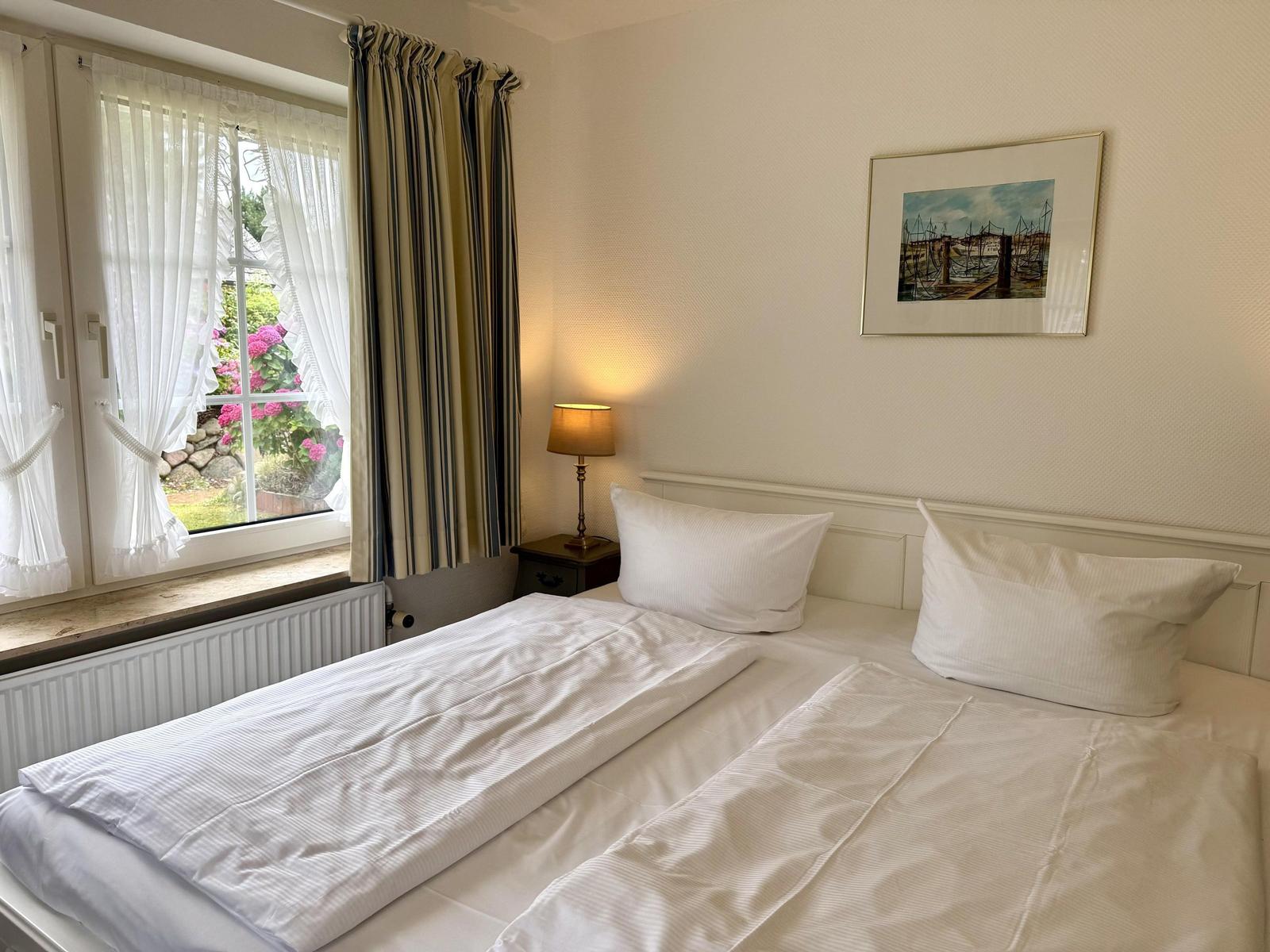 Bedroom with white double bed, bedside lamp and window facing the garden.