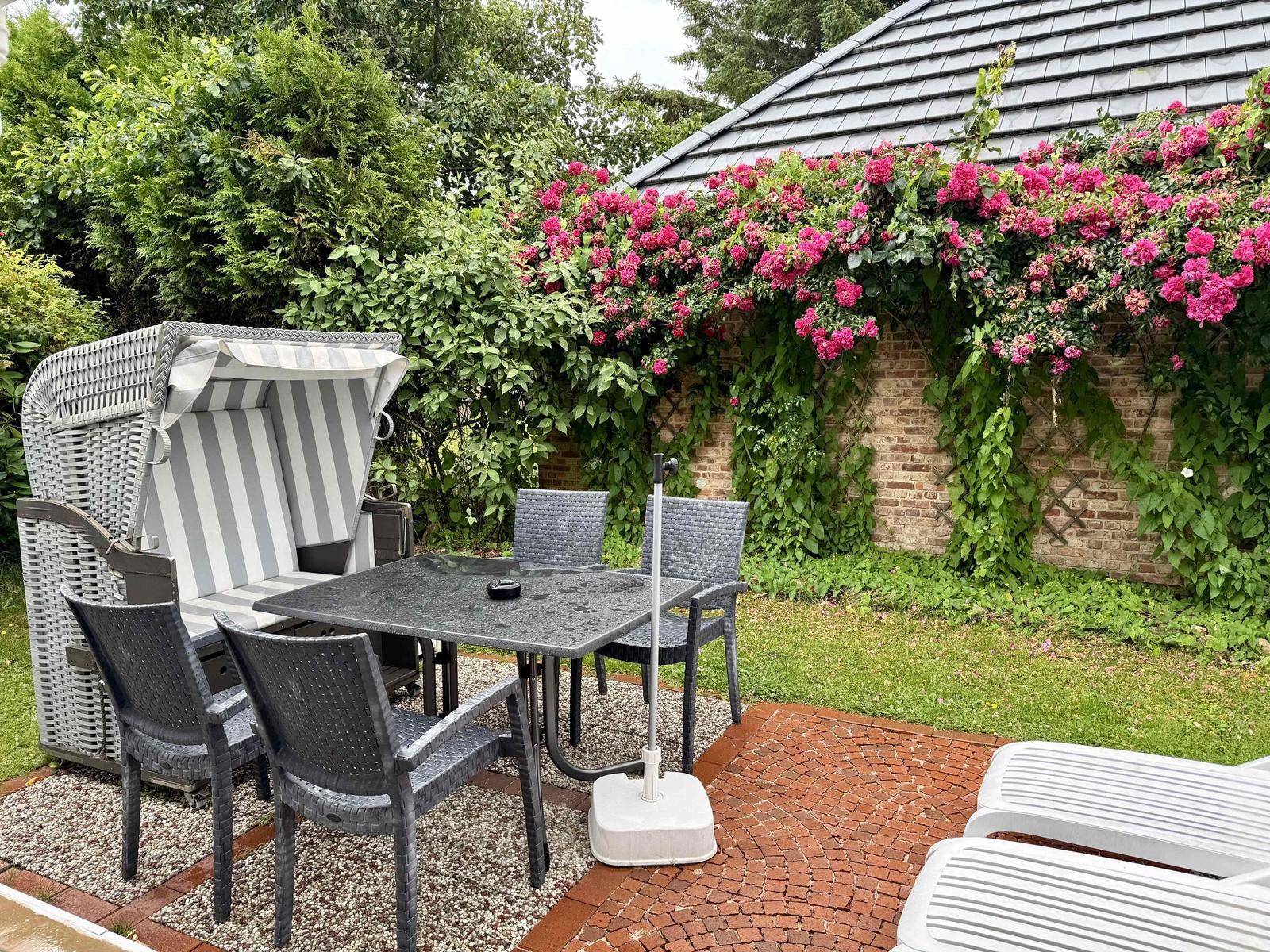 Terrace with grey beach chair, dining set and roses on the brick wall.