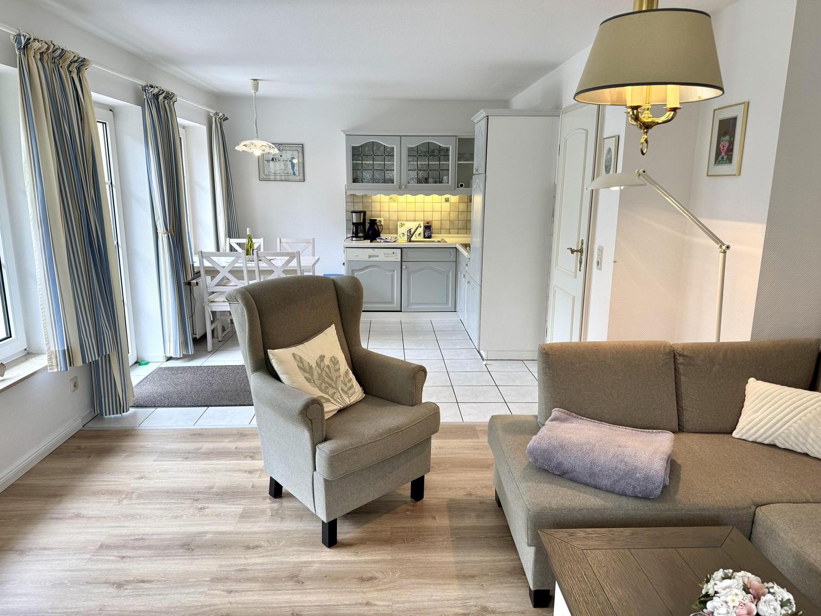 Living area with armchair, sofa, white dining table and kitchen with grey cabinets.