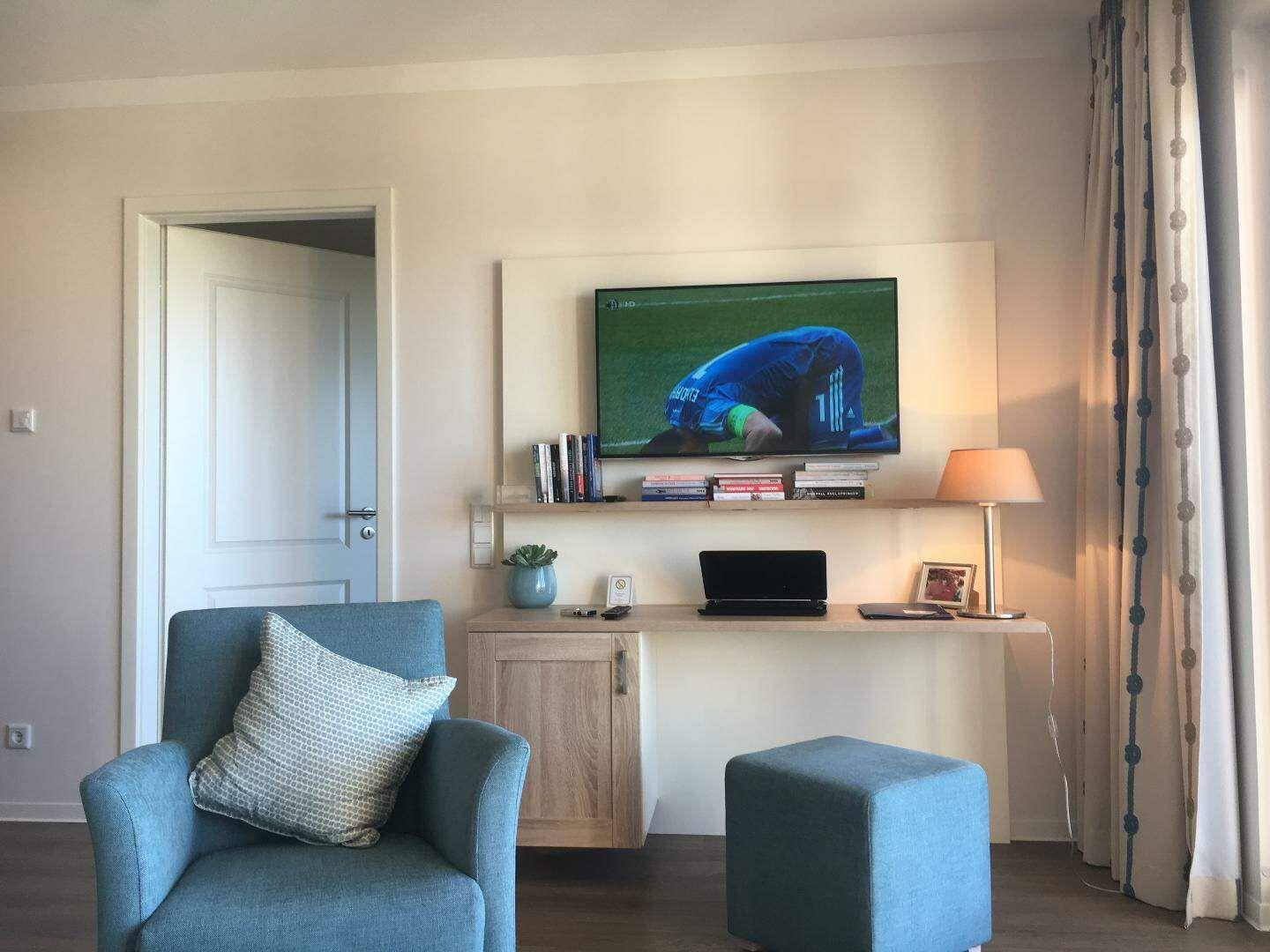 Ein Raum mit blauem Sessel, Fernseher und Schreibtisch.