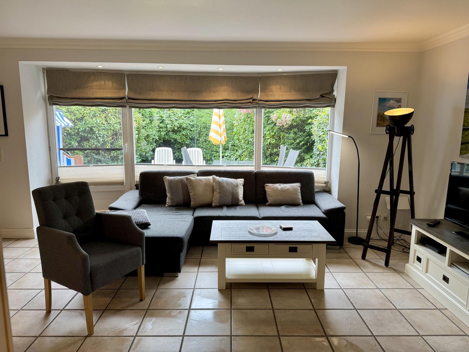Wohnzimmer mit dunklem Ecksofa, hellem Couchtisch und Fenster zum Garten.